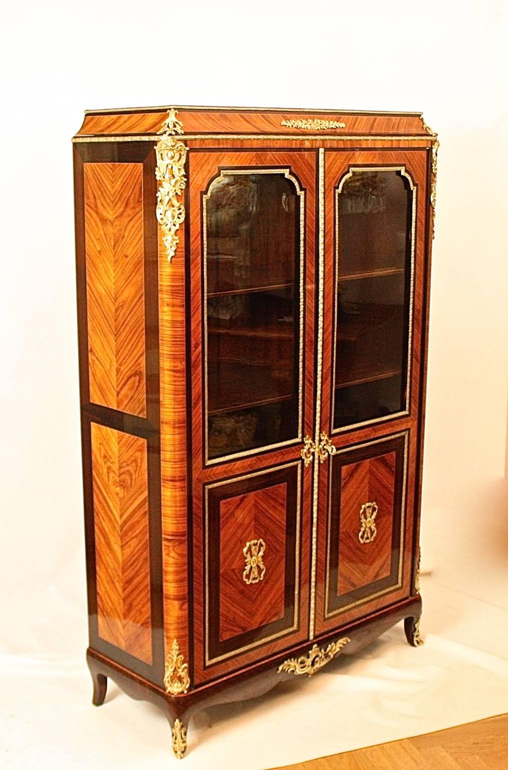 A 19th century Napoleon III Kingwood and Amaranth Vitrine/ Bibiotheque in the Louis XV/XVI transitional style, the veneered top above an arched cornice with central and corner gilt bronze mounts, enclosed by a pair of glazed quarter veneered panel