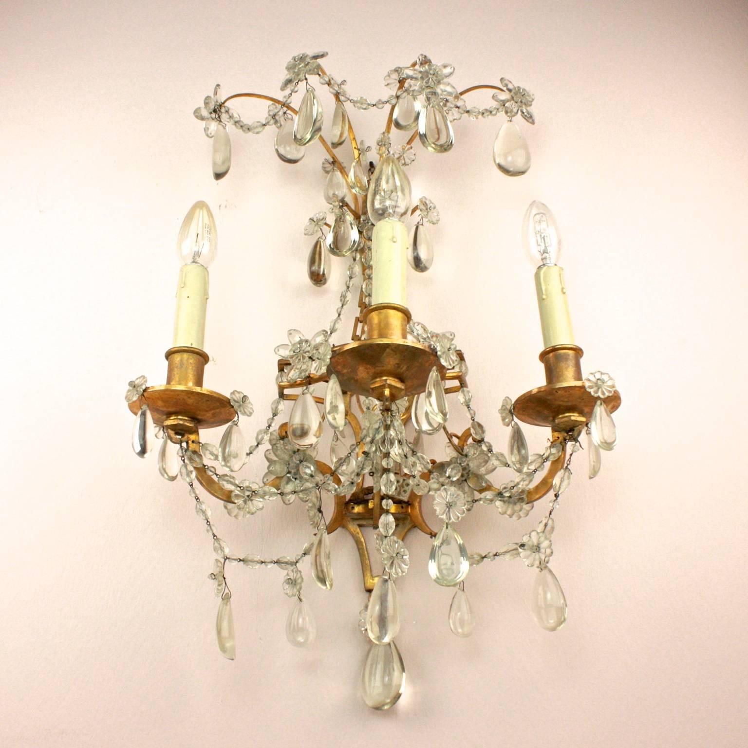 Coppia di applique a tre rami in stile Luigi XVI della Maison Bagues, ciascuna con una serie di teste di fiori sulla parte superiore, con la piastra posteriore che emette tre bracci di candele a forma di S appesi con gocce e fiori di cristallo