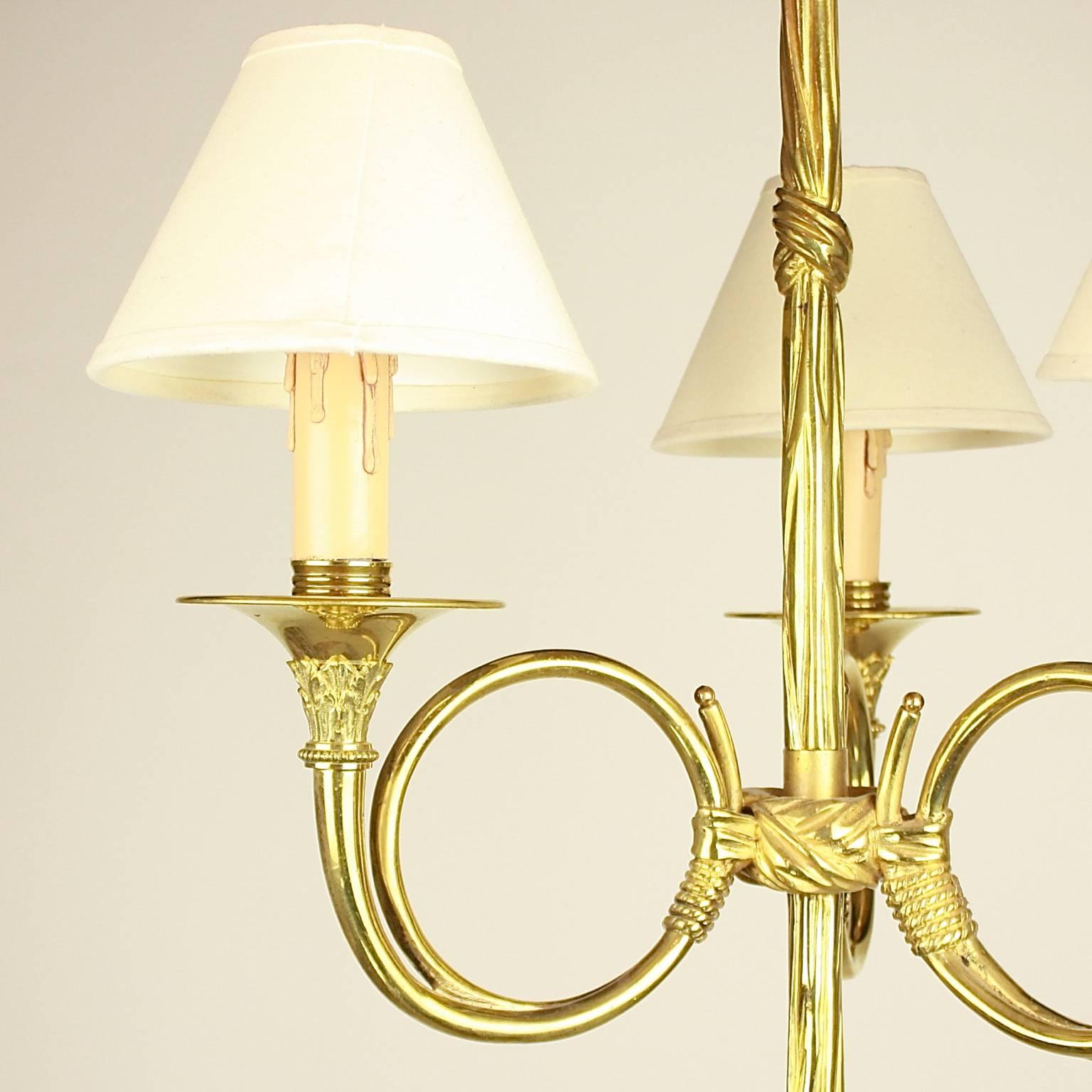 A bronze three-light 'hunting horn' chandelier made by Maison Baguès. The central baluster in the shape of drapery issuing three bugle-form arms terminating in circular wax pans and candle-form lights, each light surmounted by a small