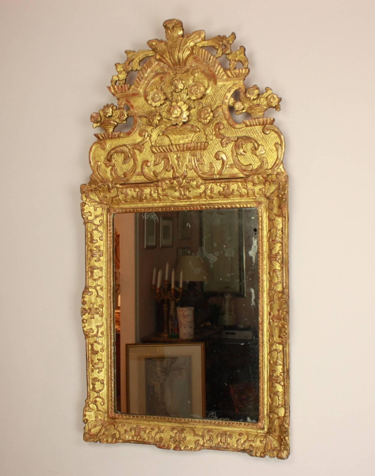 An early 18th century Regence giltwood mirror with a rectangular plate within a conforming frame adorned with a carved gadrooning border and interlaced scrolls, acanthus, cabochons, foliate and trellis cartouches on a diapered background. The
