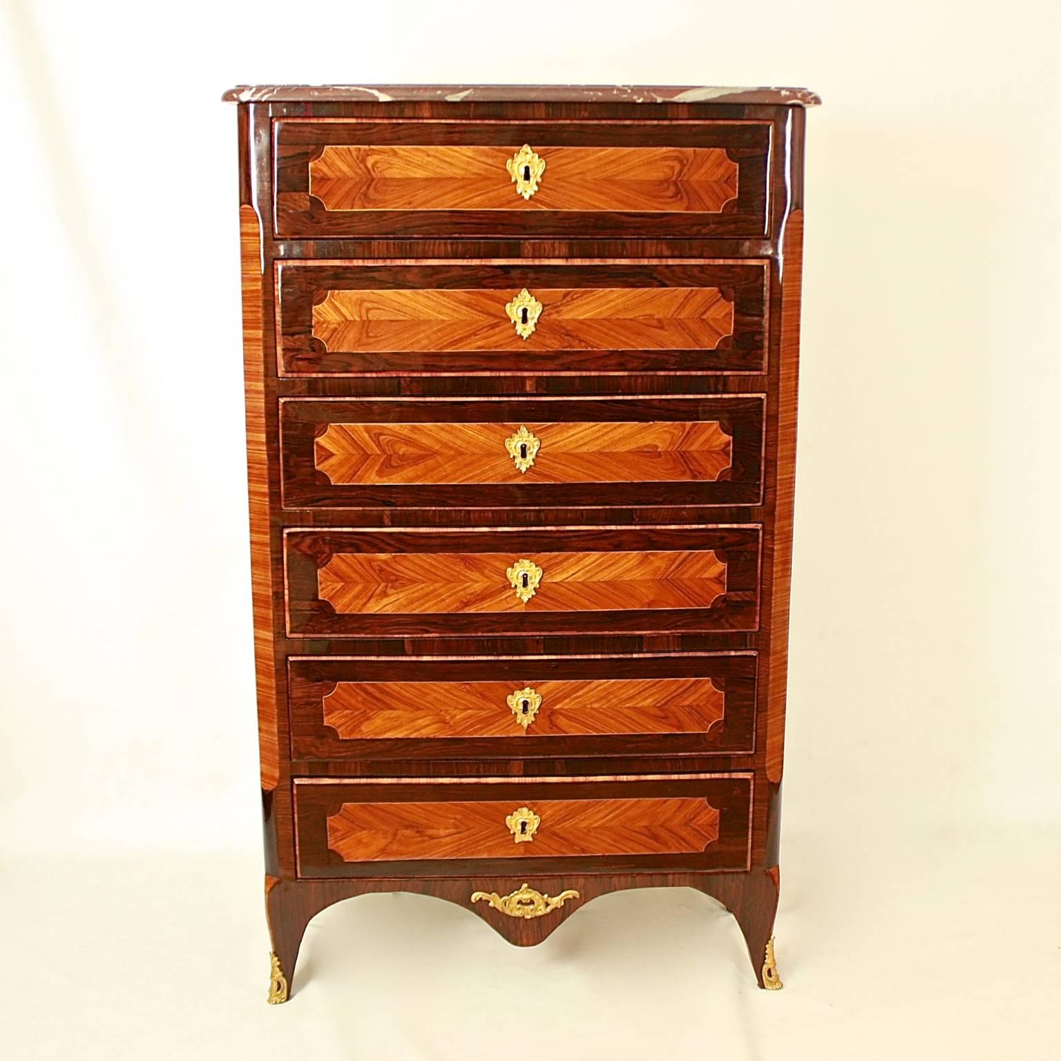 A French Louis XV tallboy or chest of drawers in the manner of Jean-Georges Schlichtig (mâitre 1765), with a moulded 'Rouge Languedoc' marble top above six drawers, each drawer veneered with cartouches of contrasting wood and fitted with foliate