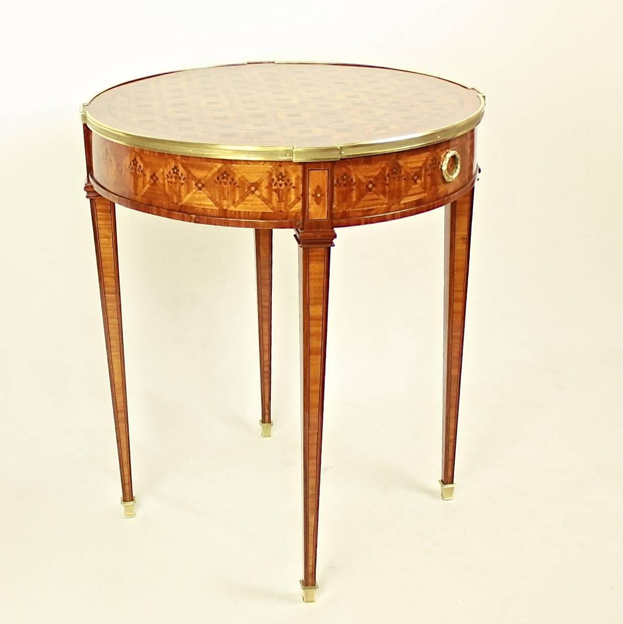 A 19th century marquetry gueridon table, the circular top with 'a' la reine' marquetry framed by a gilt bronze 'mille raie' surround above a trellis frieze containing a drawer. The table is raised on four square crossbanded tapering legs with gilt