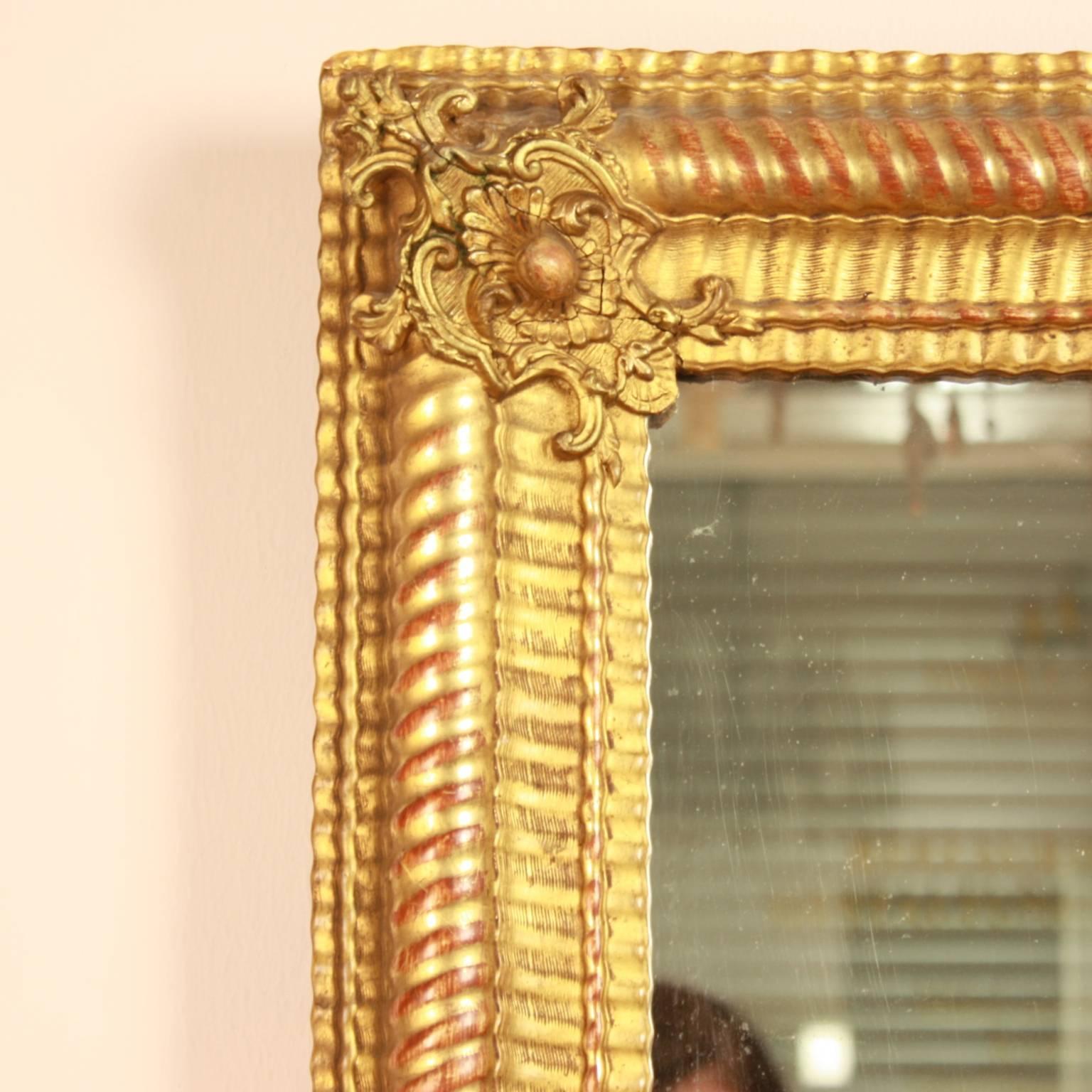Large 19th century Baroque style wall mirror of rectangular shape with fine corner cartouches, the frame as such of undulating contour with a rope design. Fine gesso carving supports the evenly wavy form of the frame. Water gilding of polished and