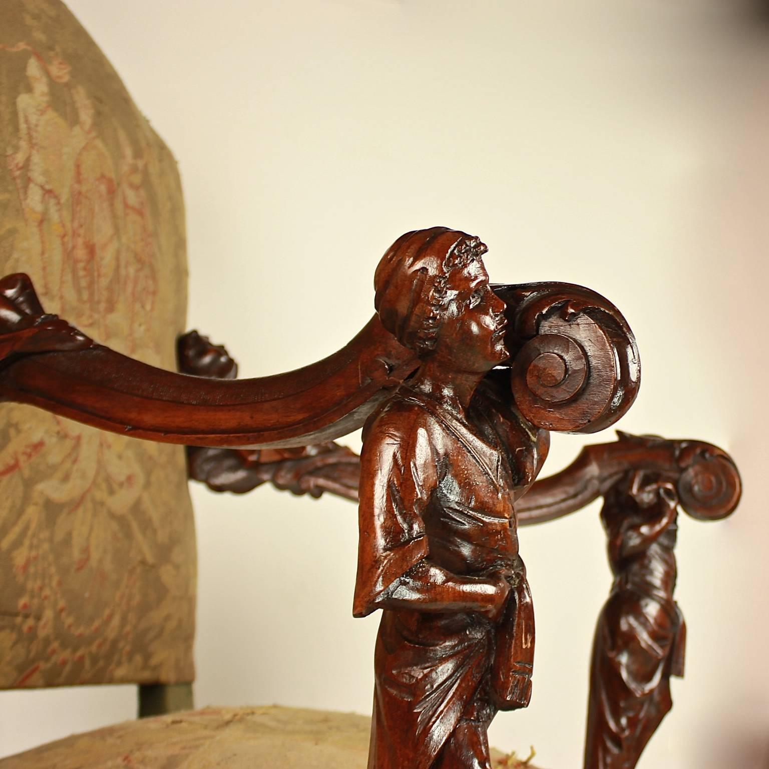 A large armchair of carved walnut, stained dark brown, with theatrically carved arm supports depicting neoclassical figures supporting the serpentine scrolling arms each carved with recumbent putti figures looking skyward. The front legs with