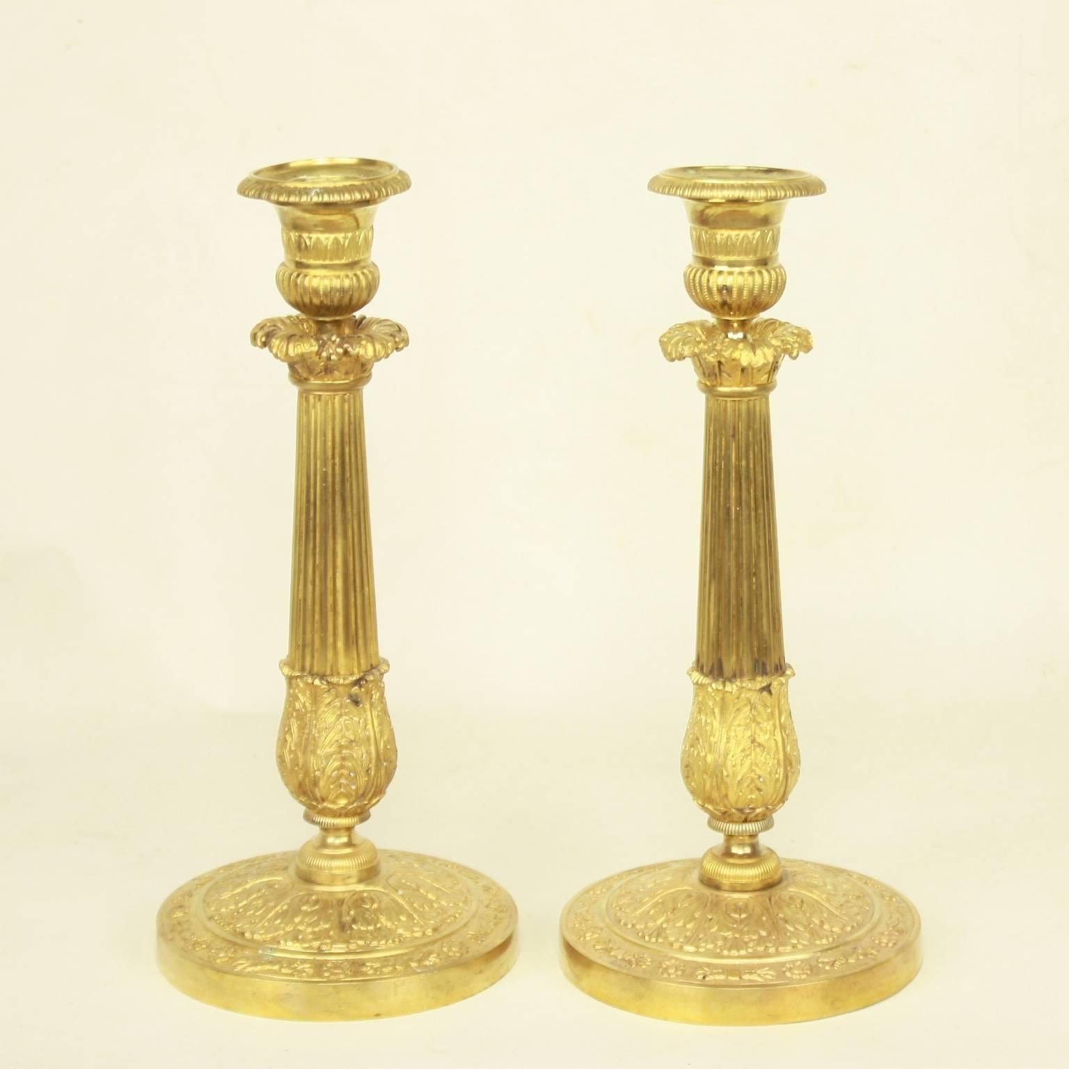 Pair of Empire gilt bronze candlesticks, each with a fluted stem, highlighted on top and bottom by finely chased foliate. The cannellure cast sockets with removable nozzles. The stem rests on a circular base accented by acanthus leaves and skirted
