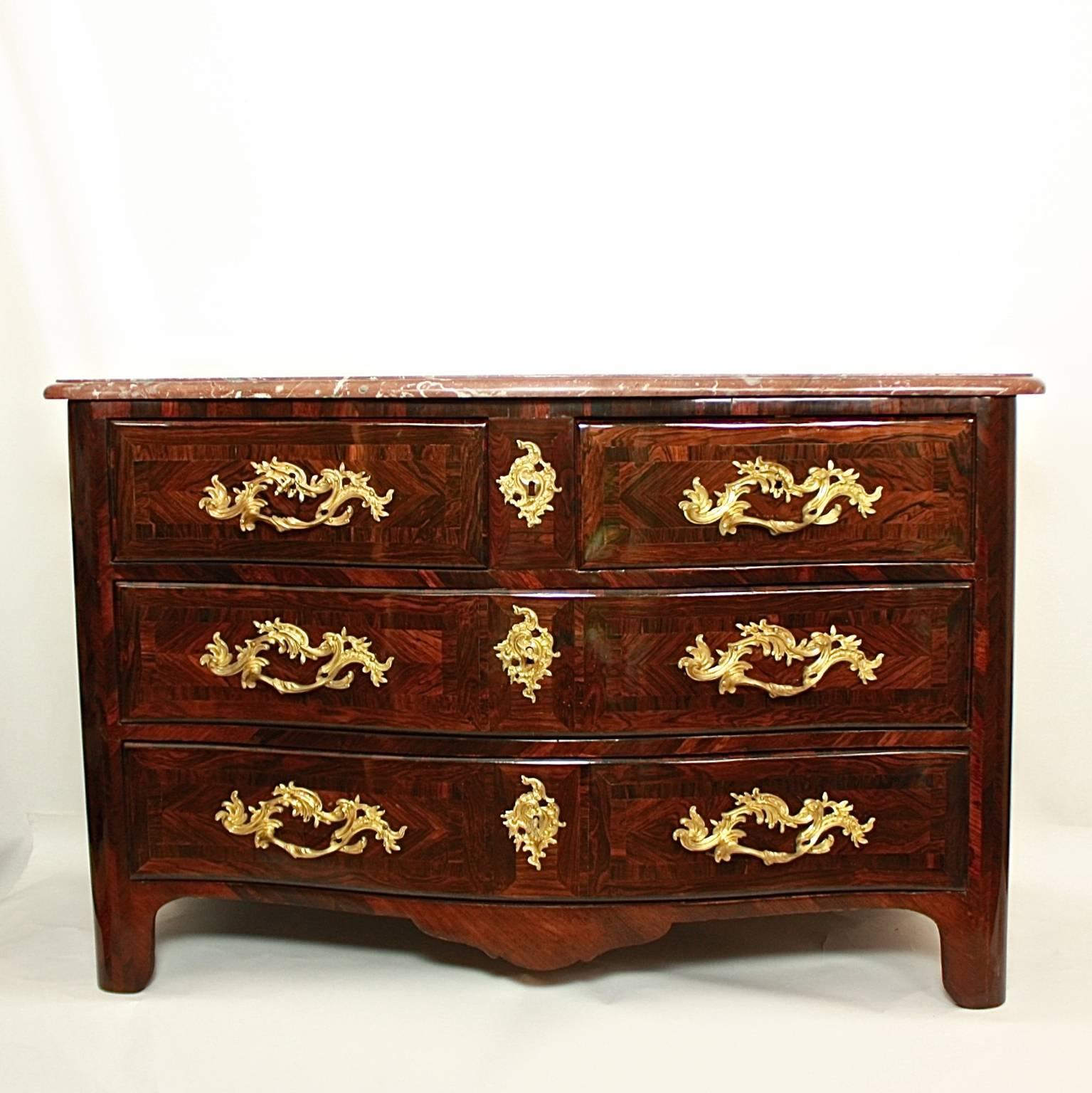 Early 18th century Regence commode or chest of drawers with rosewood parquetry and a moulded russet marble top (griotte de Belgique) above a serpentine shaped front with two long drawers below and two short drawers above, with rounded corners, on
