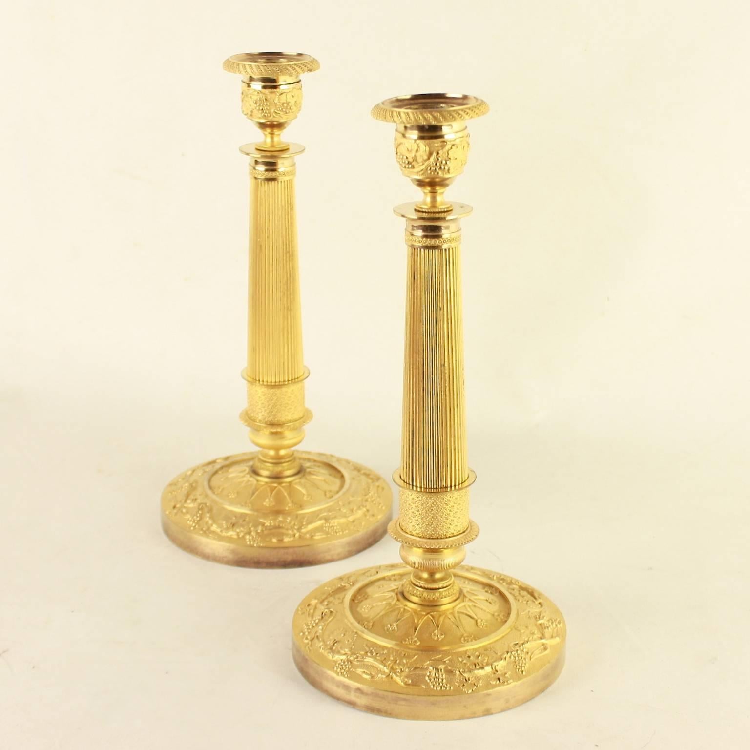 Pair of Empire ormolu candlesticks with beaded and finely chased drip pans, nozzles with vine leaves, grapes and tendrils on a fluted shaft resting on a circular base with a doomed foot. The base again finely chased with vine decoration. The decor