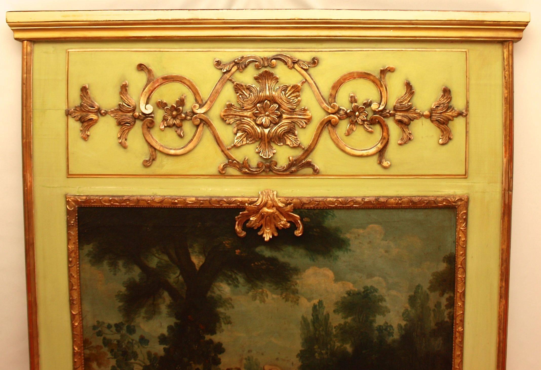 An 18th century trumeau mirror with a mirror plate framed by a giltwood border surmounted by an oil painting and a giltwood carved freeze of stylized foliate ornaments and strapwork on a light green background. 
The inset painting of a 'fe^te