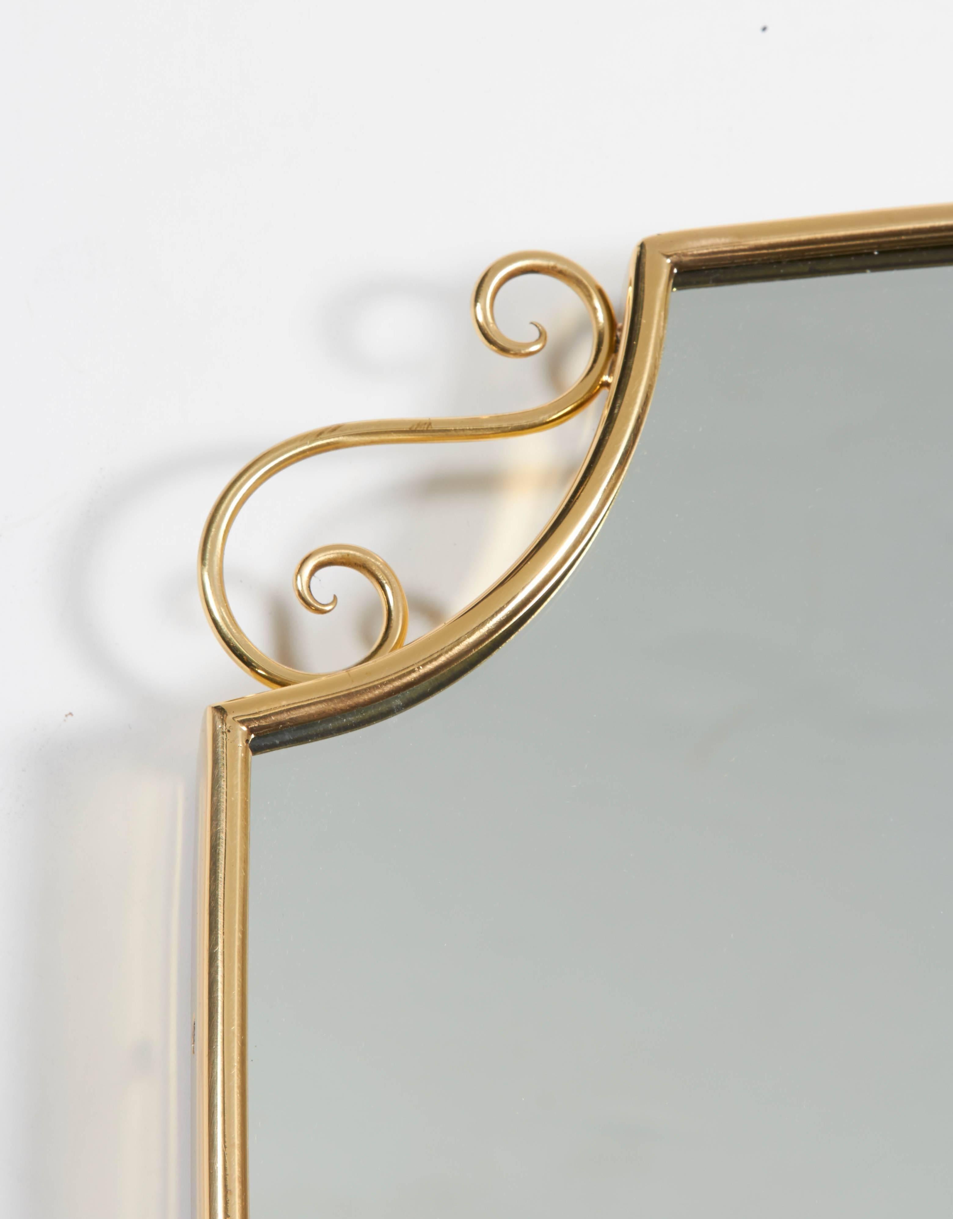 A lovely pair of 1950s, Italian shield shape brass frame mirrors. Each frame handmade with top multi loop and side scroll accents. One mirror measures 18.25" wide and 20.5" high. The second mirror measures 18.5" wide and 20.5"