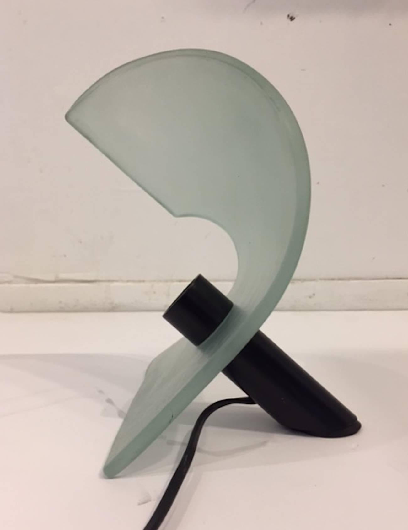 A beautifully minimal design and sculptural petite table lamp by well know Italian lighting house De Majo of Murano, circa 1980, the lamp consists of a satin finish glass panel that curls around and over the light bulb. The shade is supported on end