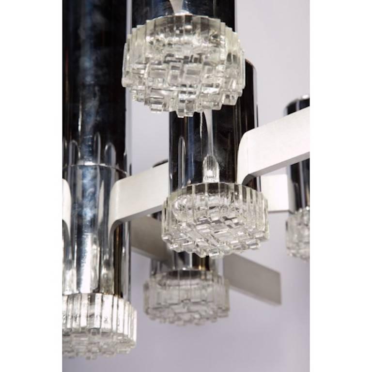 Abstract 1970s chandelier designed by Gaetano Sciolari for his Italian family's noted lighting company of the same last name. Polished chrome metal tubes house each bulb and are capped by a molded geometric pattern glass cover. Brushed finish