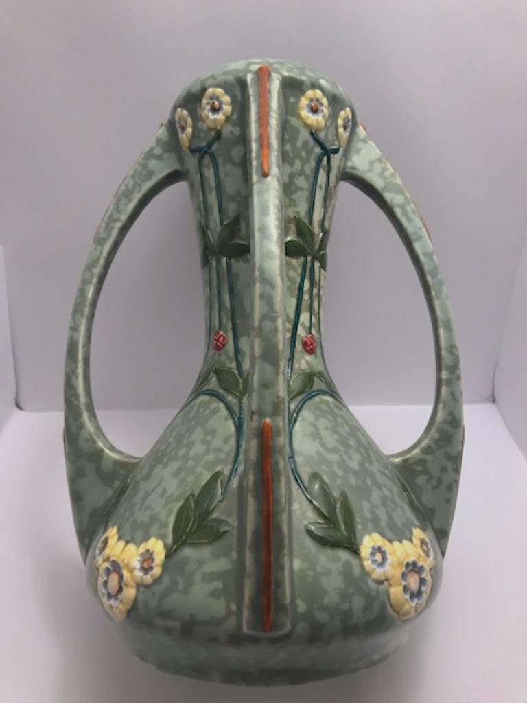 A lovely circa 1918 Art Nouveau ceramic vase by the Czechoslovakian ceramic and porcelain company Royal Dux. The body has a semi matte mottled two tone green glaze. The floral decoration is molded into the vase and hand-painted in yellow, red and