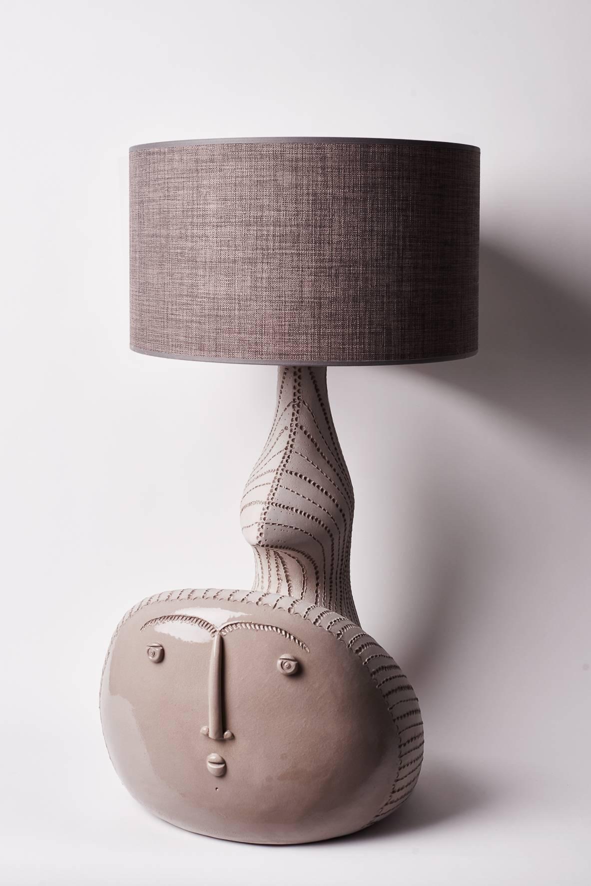 A sculptural and biomorphic shaped lamp-base or sculpture in natural warm grey stoneware, stylized form, decorated on front with a stylized visage incised and over-glazed in shiny grey.
One of a kind handmade piece, signed by the French ceramicist