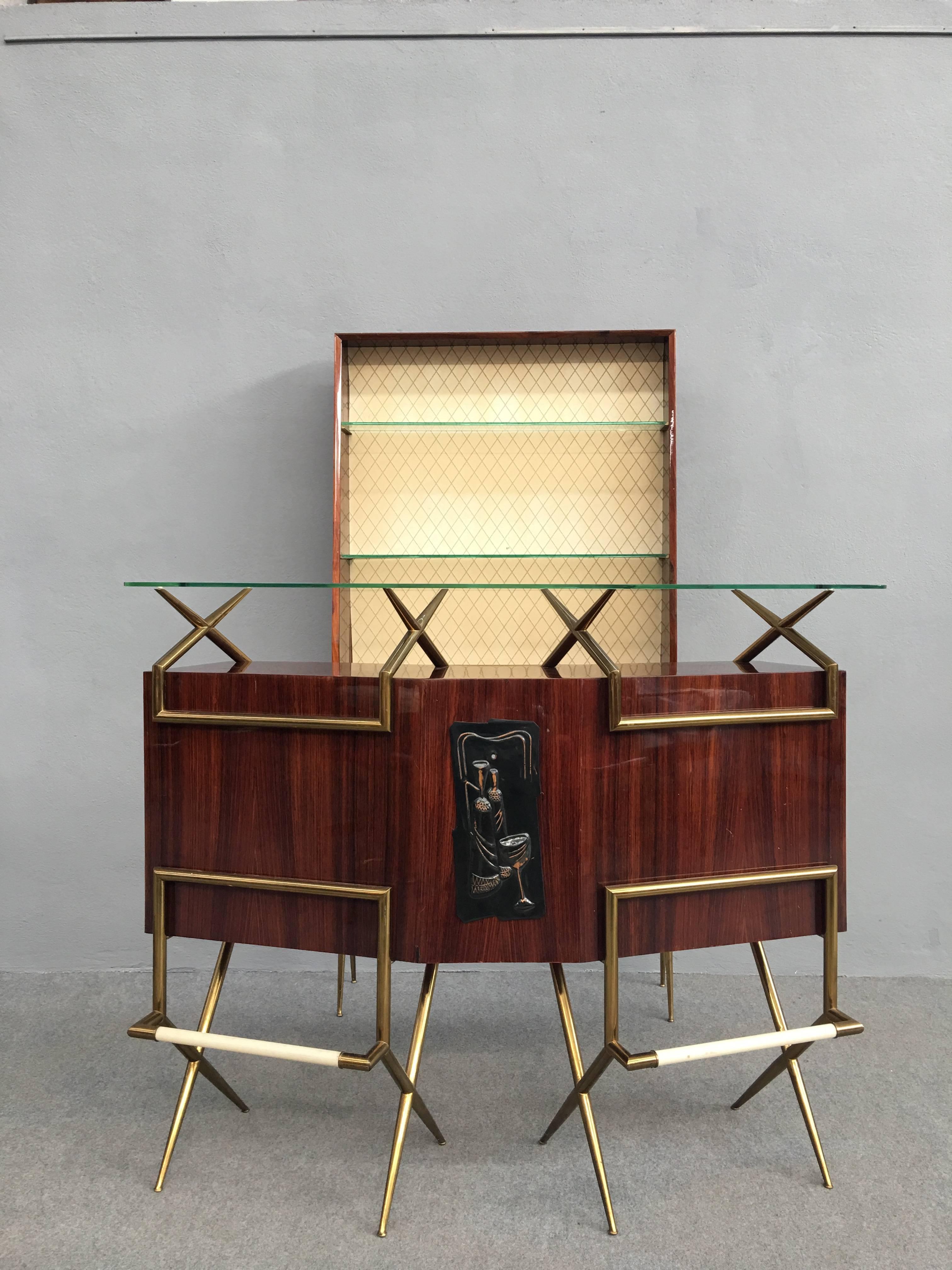 Mid-Century bar set: Standing bar, standalone case and two stools.
High gloss laquered mahogany, brass legs and glass top. Bronze art piece in the middle.
Open compartments and drawers.
Case piece with two shelves measures 180cm height, depth 25