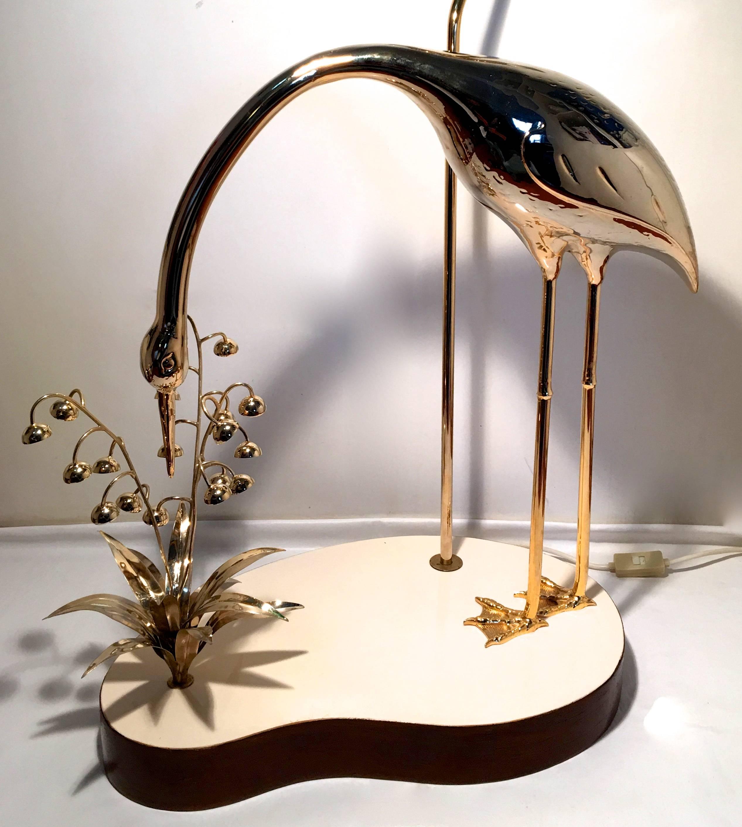 Glamorous floor lamp with a gold colored sculpture of a heron sniffing a blossoming flower.
With very nice detail. The bird stands on a kidney shaped resin base with a mahogany lining. The lamp has two light fittings and any shade can be mounted