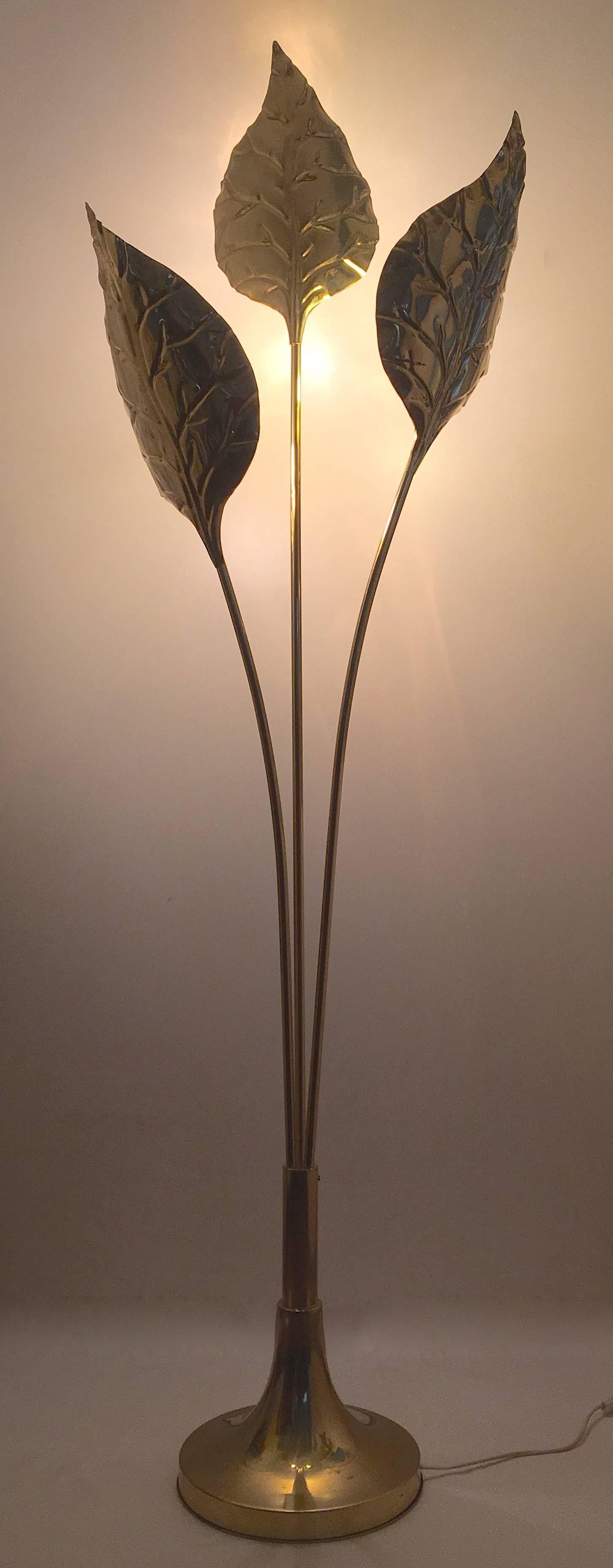 A brass floor lamp with three arms that rise from an elegant base. Its three brass leaves shade a bulb each, Italy, circa 1970.