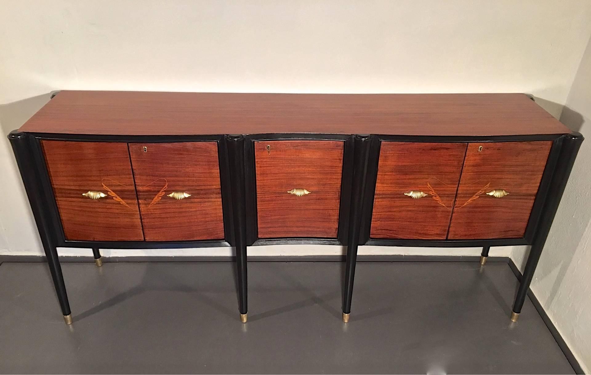 An Italian credenza or sideboard with double doors on the side and a single door in the middle. Sculptural details such as the curved lining on the front and the tapered ebonized legs with brass feet. Decorative doorhandles and beautifully detailed