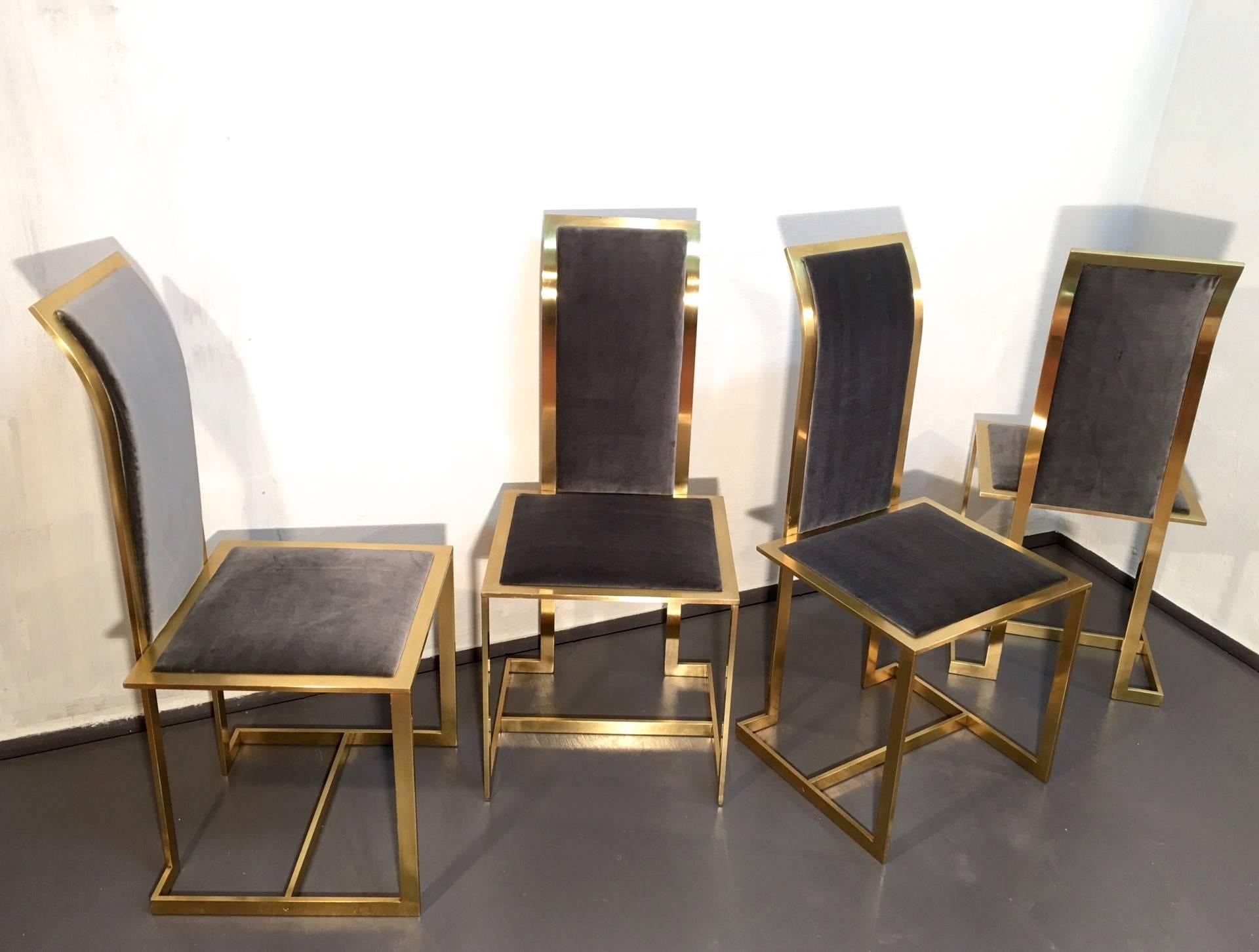 Set of four brass dining chairs with dark grey velvet upholstering and articulate designed brass body. Tall and slightly angled backs that are joined on rectangular seatings with a geometric base