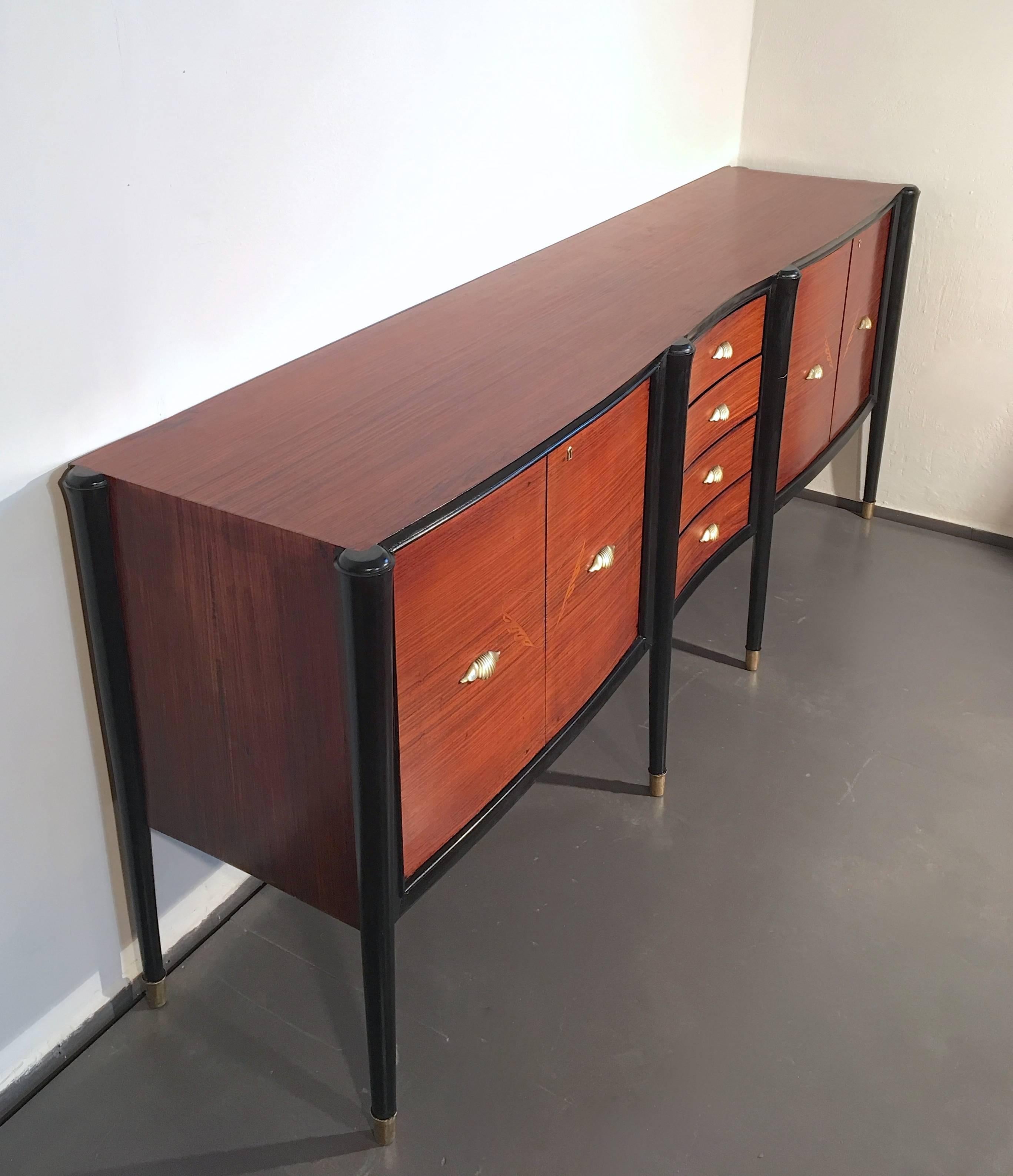 Elegant Italian credenza with a set of drawers and decorated doors on either side. Sculptural design and tapered legs. Brass details. This piece can be combined with a similar credenza in the collection.