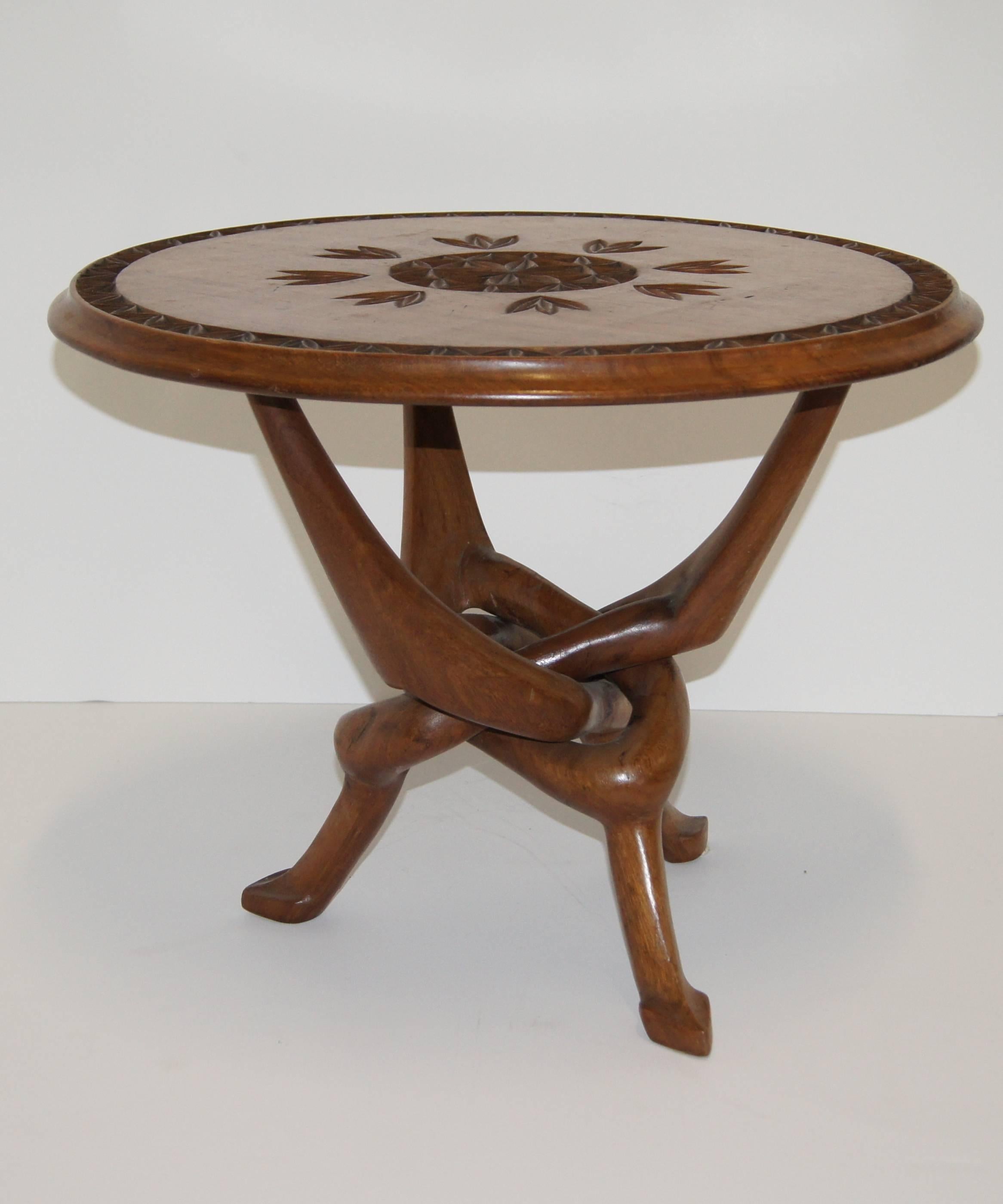 Beautifully carved tripod table with entangled legs that form a knot. Floral carved pattern in the center and side of the tabletop. Rimmed edge.
  