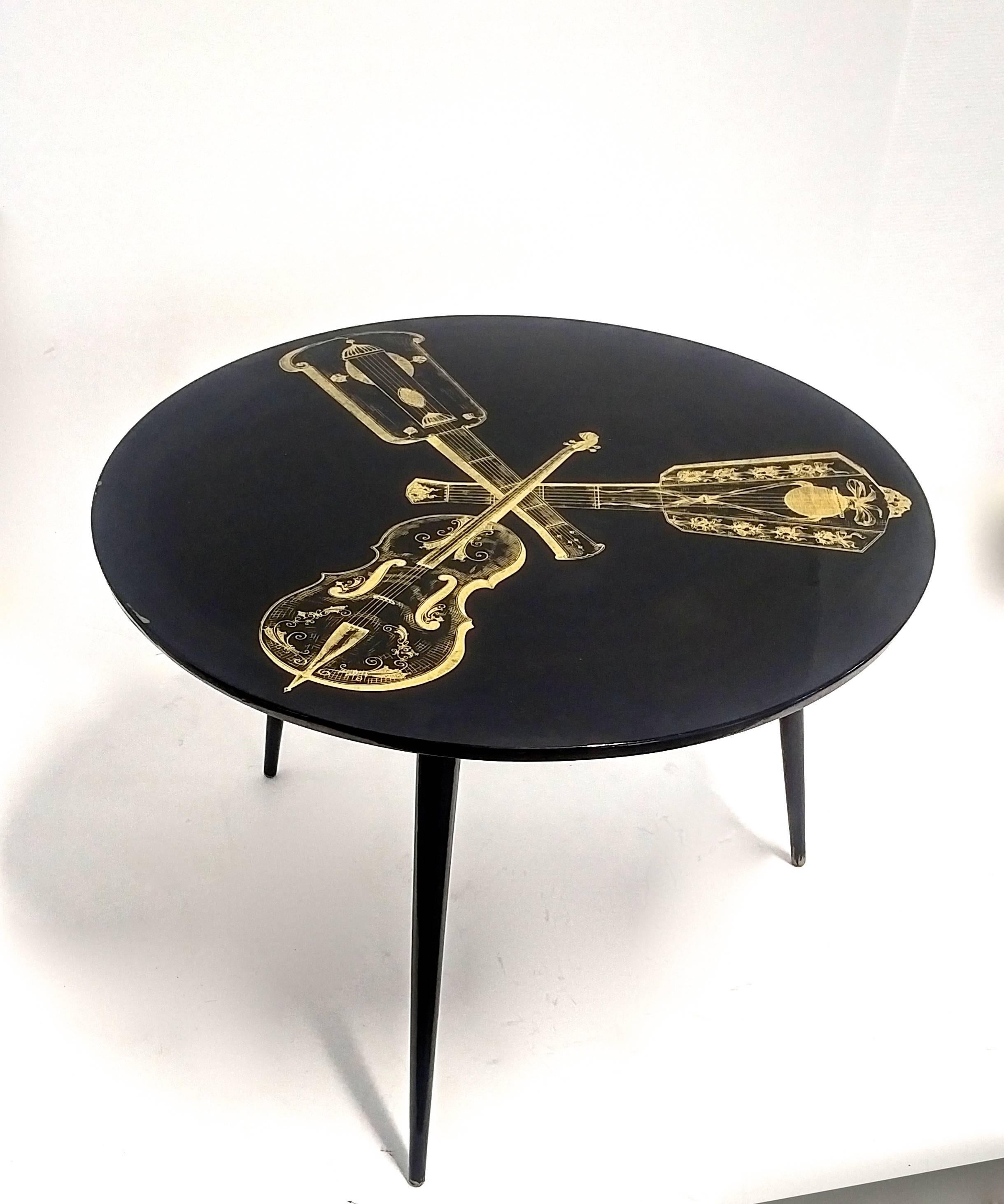 Decorative Italian Mid-Century side or cocktail table with black lacquer top and gold painting of string instruments in the style of Piero Fornasetti.
The legs can be dismounted from the top.