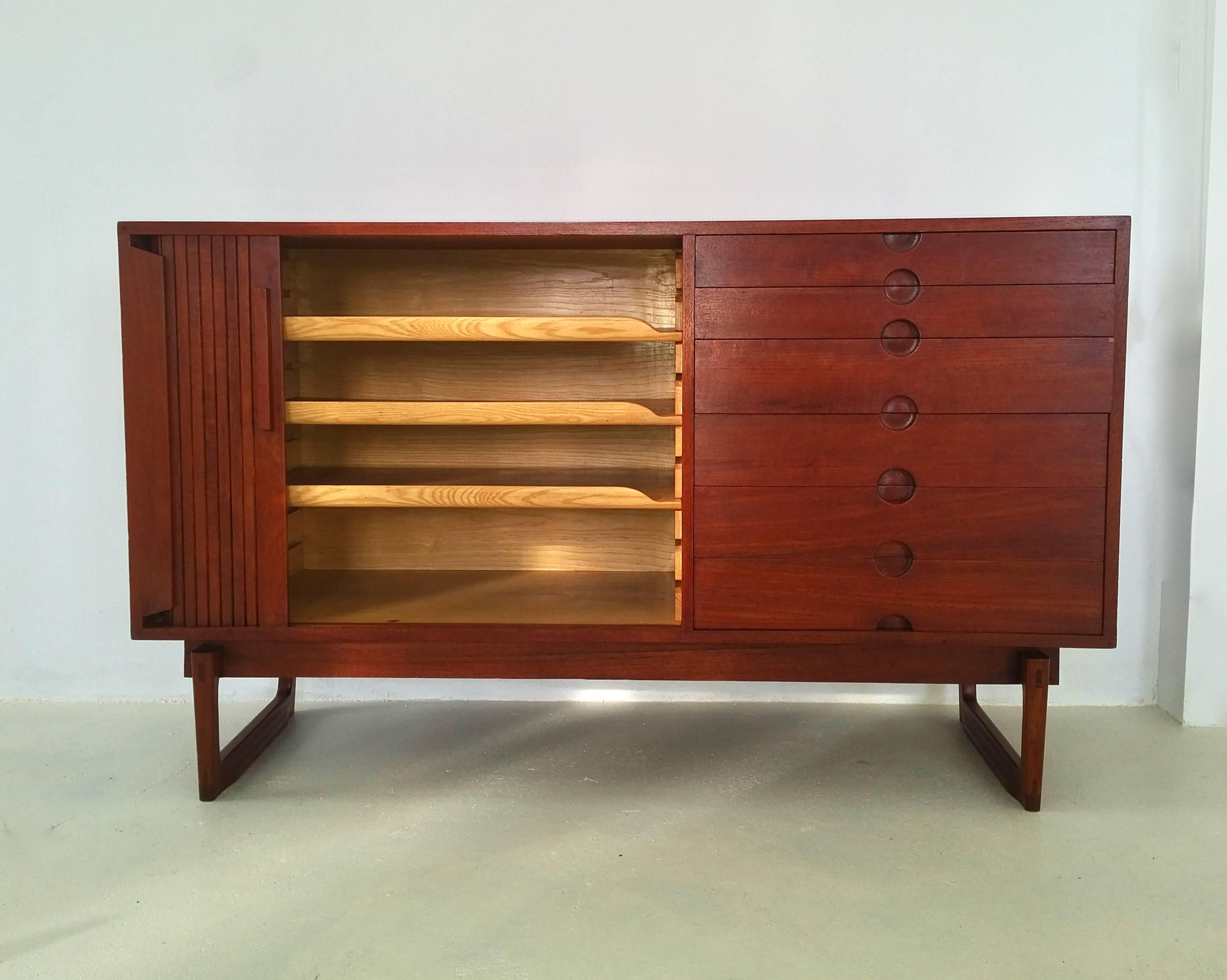 A high quality made credenza with six drawers and a tambour sliding door which hides three ashwood trays that can be taken out and put on different heights inside. Beautiful details such as the joints, the bicolored feet and the curved edges on the