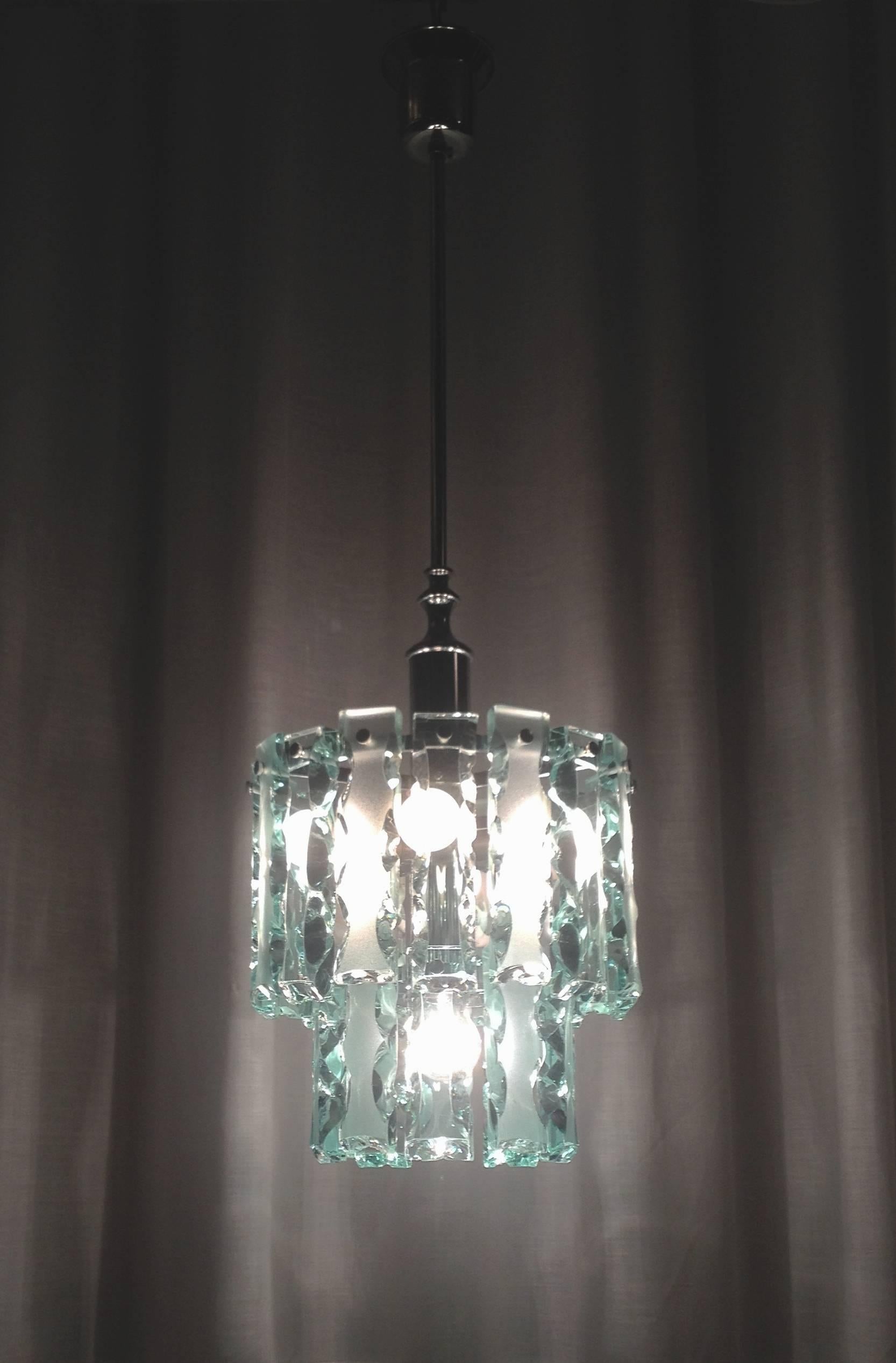 this Pendant features  two rows of hand chiseled frosted glass hanging from a chrome plated frame with small chromed knobs and suits 6 bulbs. 
Zero Quattro chandeliers were made for only a short time. The Milan based company  produced some