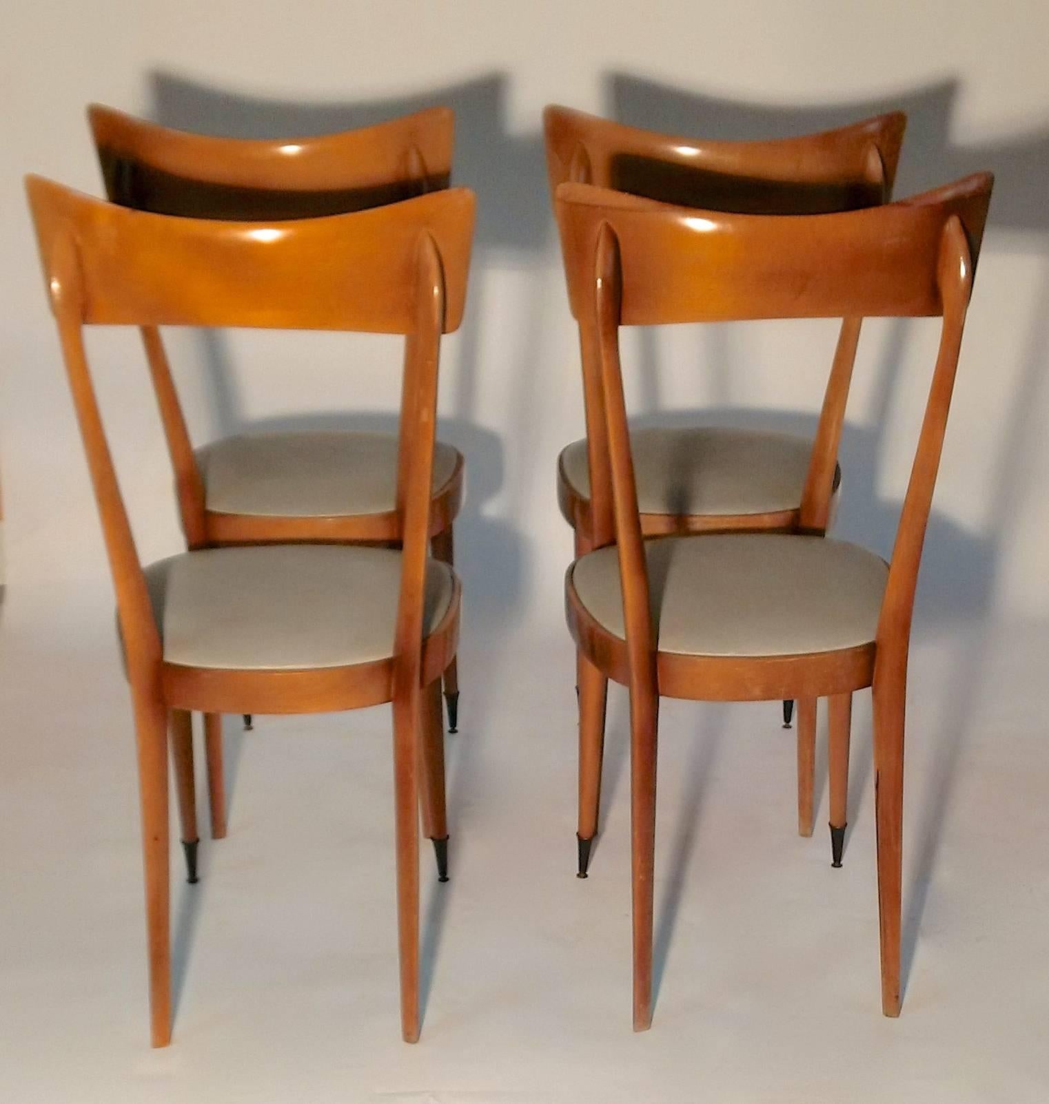 A set of four wooden dining chairs with elegant sculptural design from Milan, circa 1950.
The front legs have brass tipped feet and the seating is in a light grey /green faux leather.