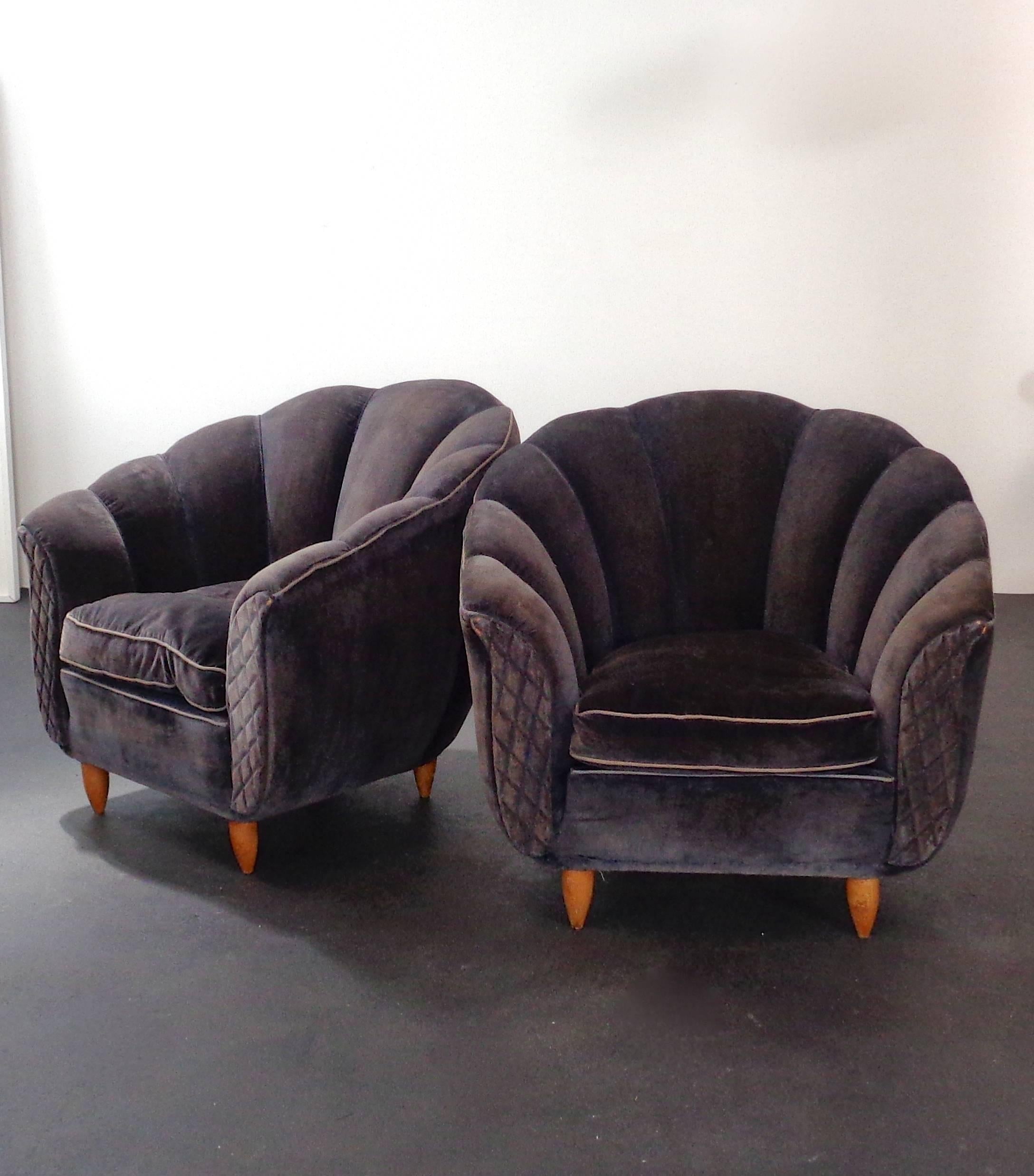 A pair of dark purple velvet coquille armchairs with wooden tapered feet and textured front of the wooden armrests.
Original fabric.