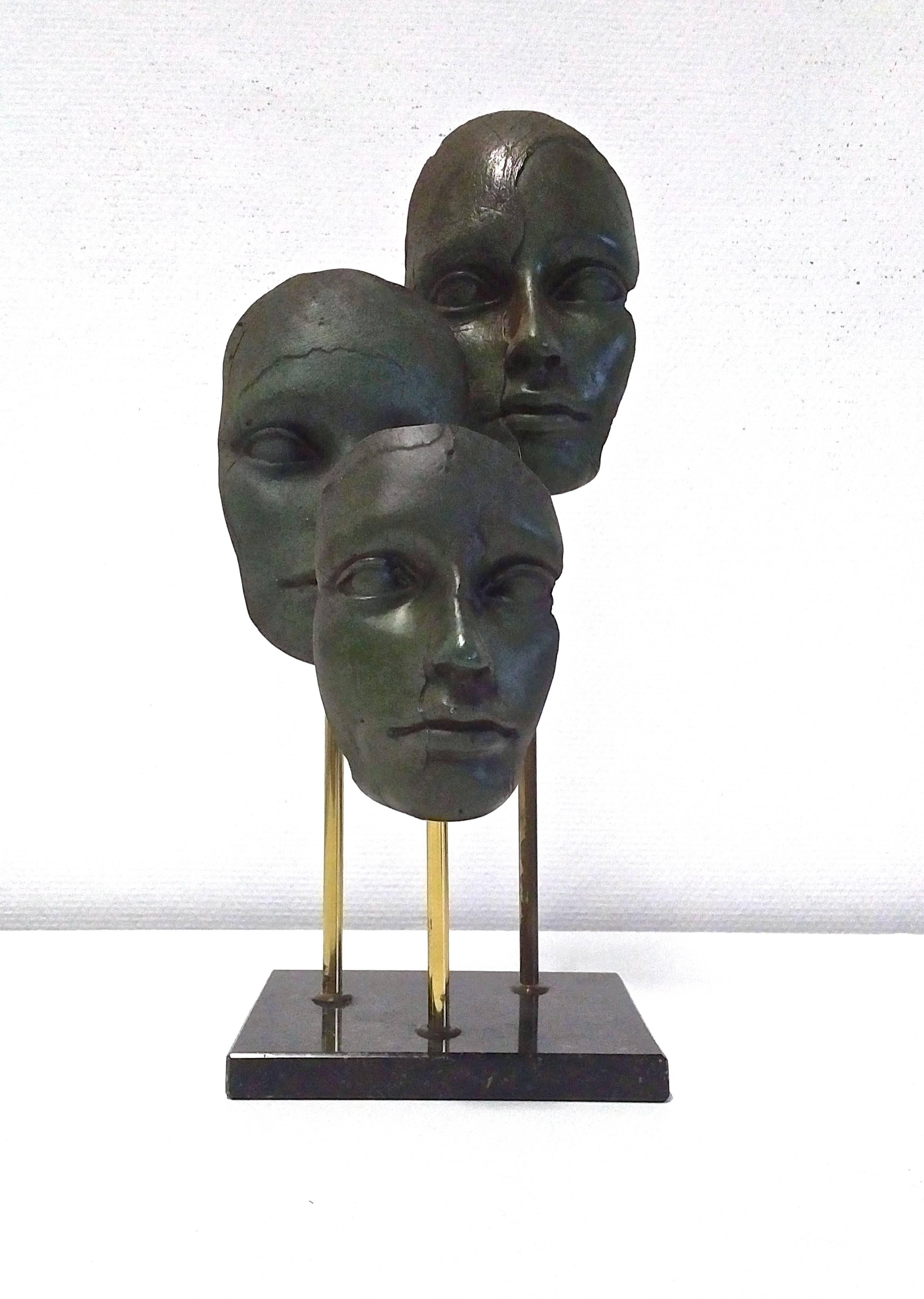 A very interesting sculpture with three faces that have a subtle change in expression. A beautiful green bronze patine. They are mounted on brass extensions that emerge from the marble base on different heights which gives it depth and drama. The