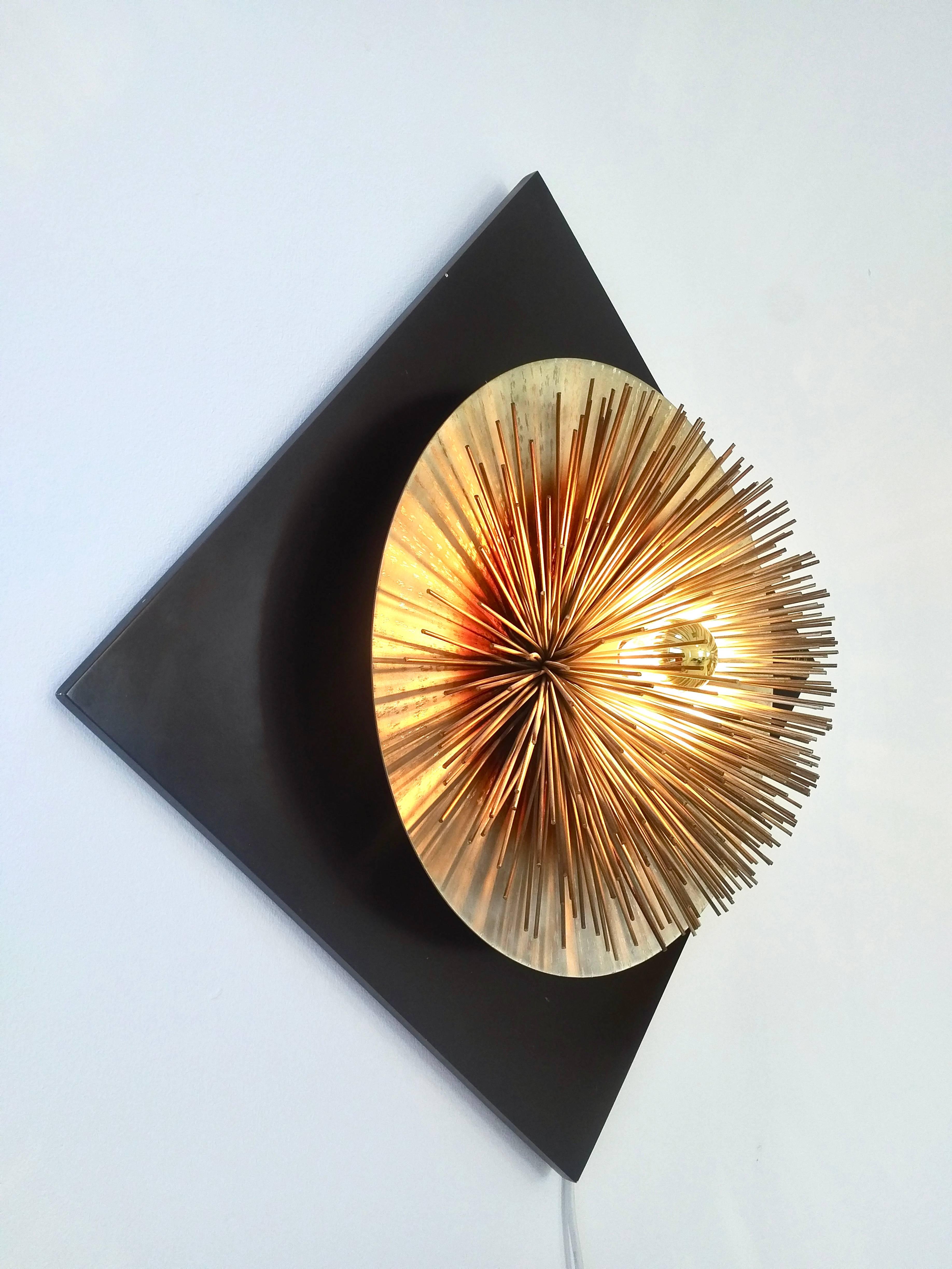 Brass and metal 'Aurora' light sculpture from the series 'Hit Proposals' ; produced between 1974-1975. This series was conceived and produced by Studio EF, Viareggio, Italy.
The brushed metal disc mounted on a lacquered wooden panel is covered in
