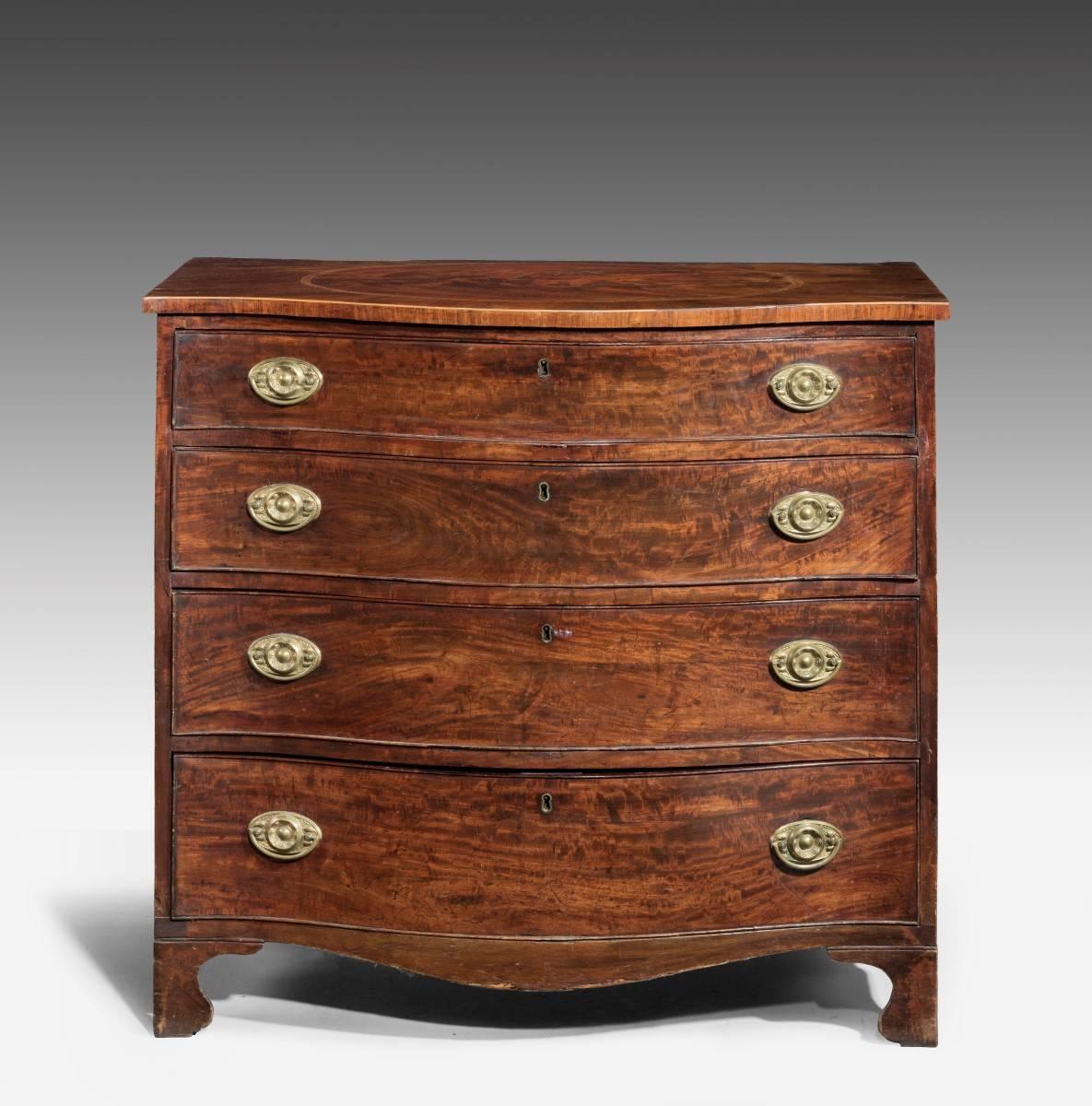 An attractive and well figured George III serpentine mahogany commode on shaped bracket feet. The top quartered and finely inlaid, with a contrasting oval centre within a Kingwood border. Period replaced handles.