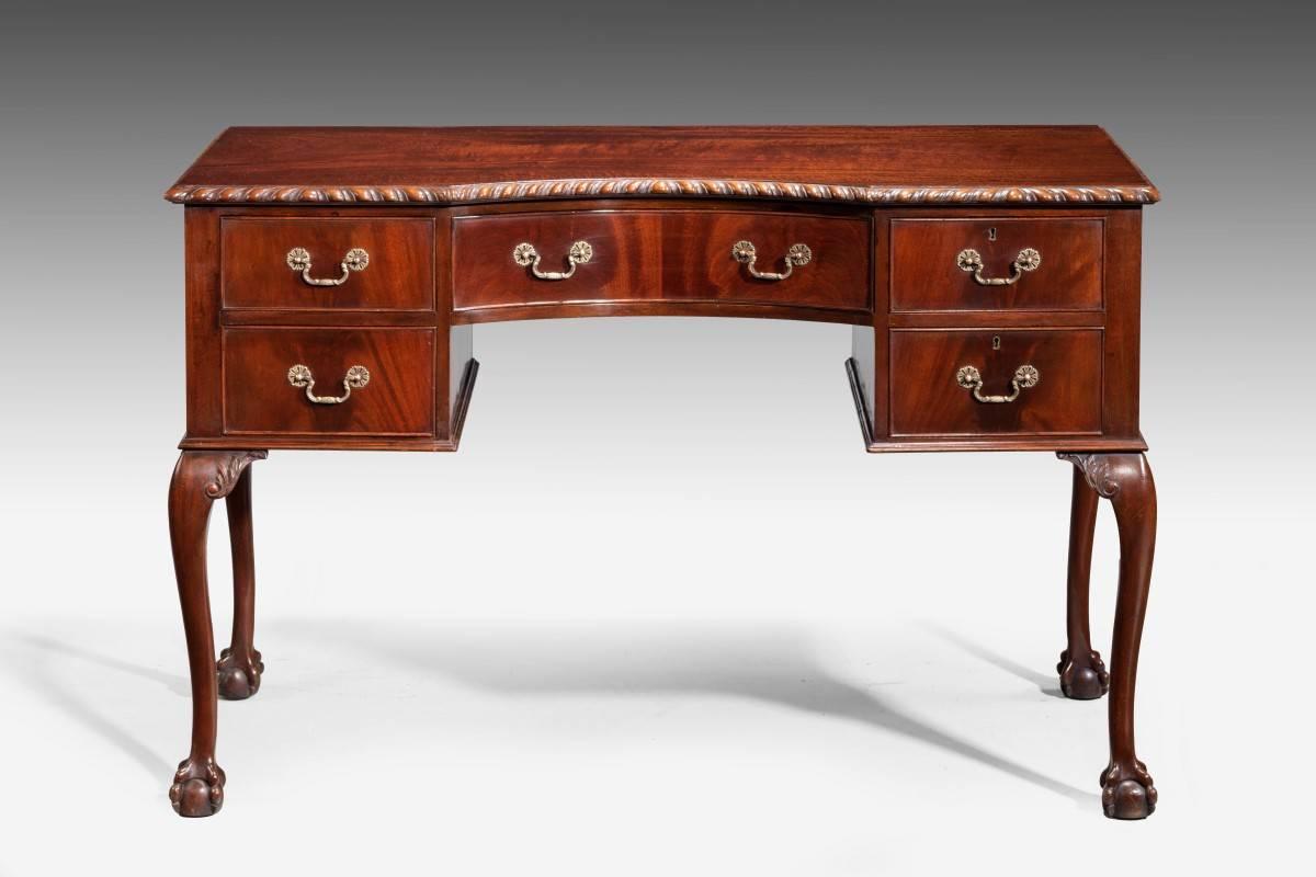 A mid-20th century mahogany desk on well-shaped cabriole supports terminating in claw and ball feet. The top edge with a continuously carved gadroon border. Original cast bronze handles.