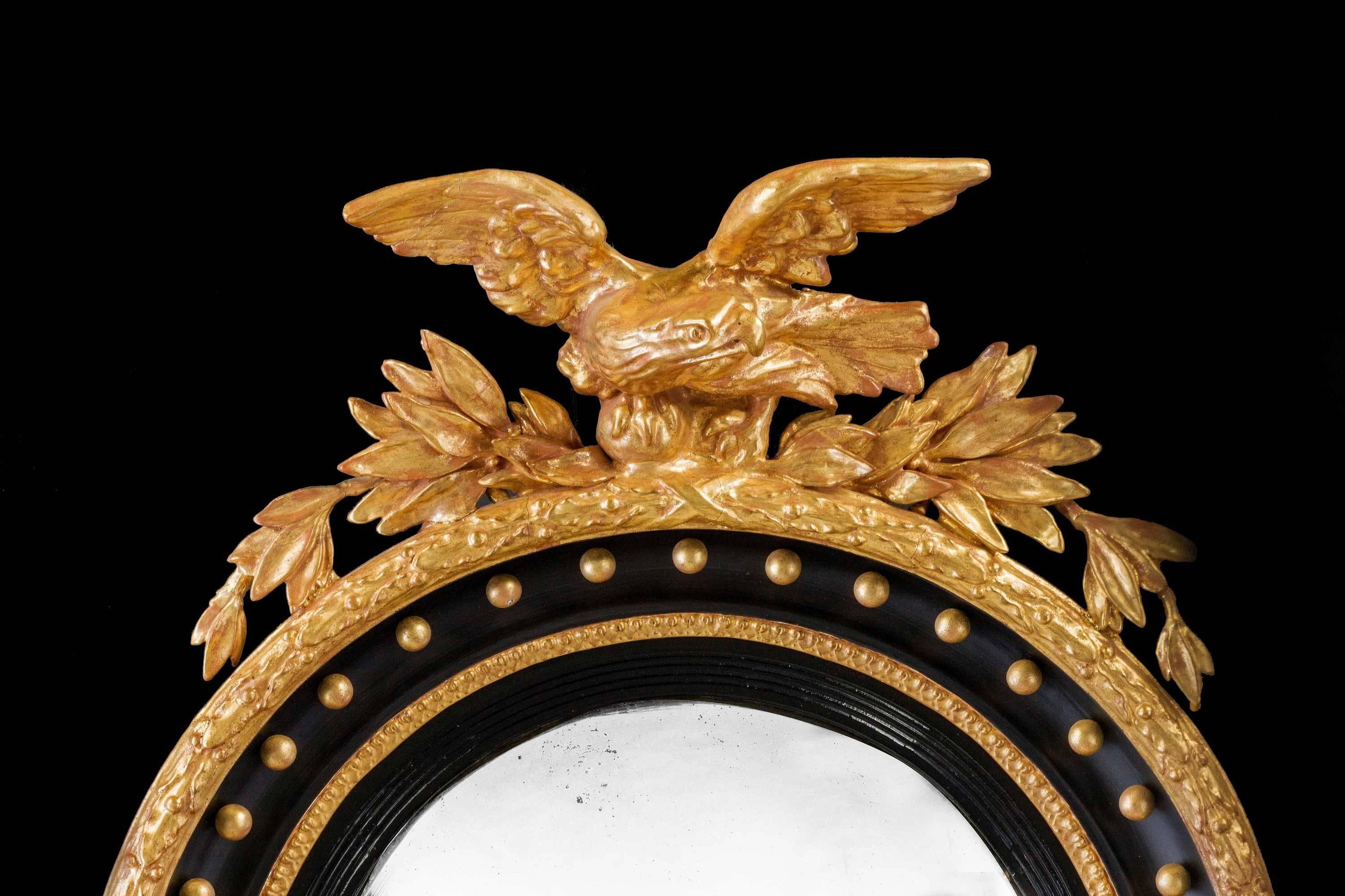 A fine giltwood and parcel gilt Regency period convex mirror, the top with a vigorously carved eagle in-flight between foliage, the inner border with decorative balls.