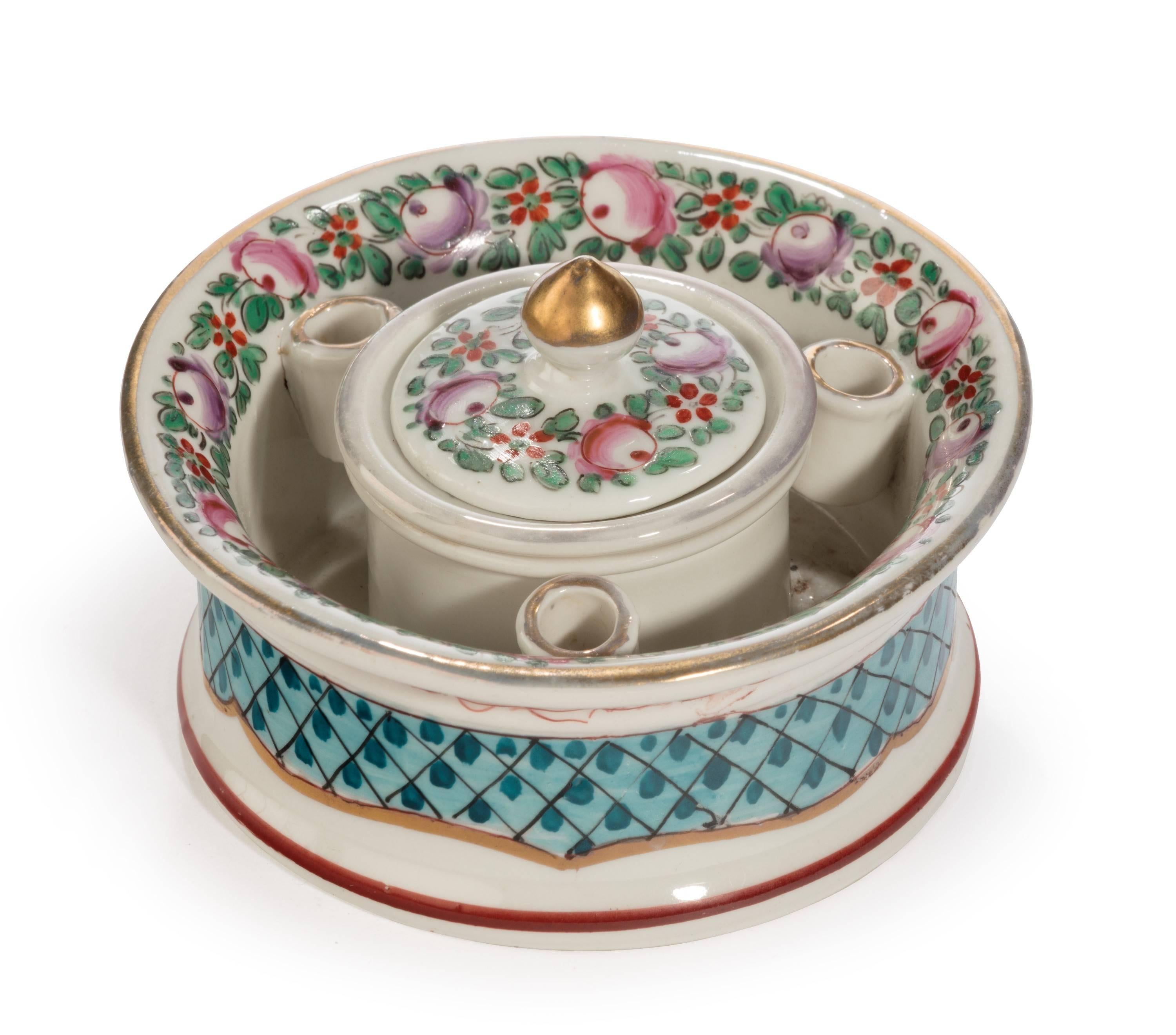 A continental porcelain inkwell retaining the liner and lid. The lid with a minor chip to the underside. The circular container also with quill holders.