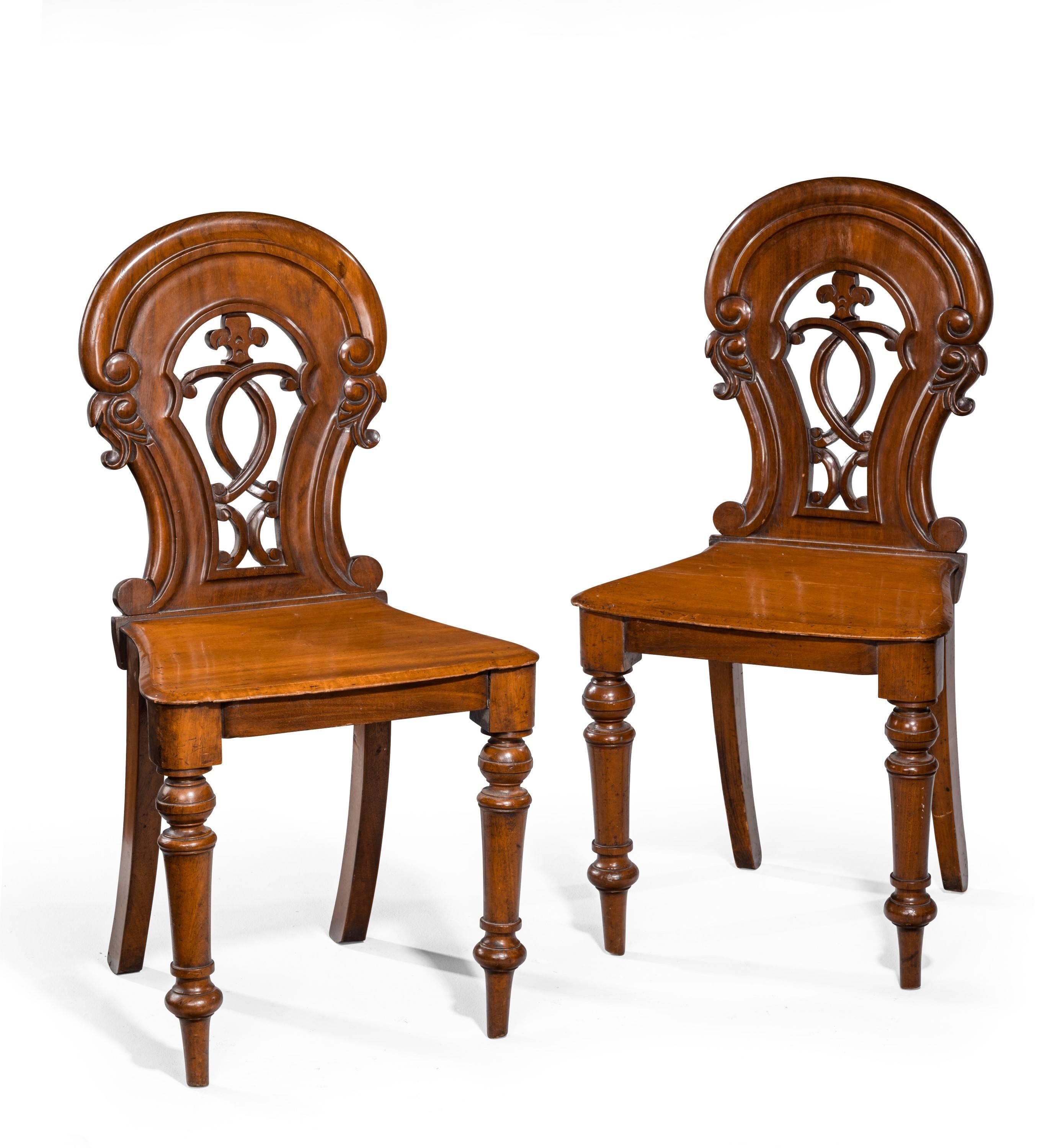 A pair of early Victorian hall chairs. Tapering square supports. The backs with carved tops over pierced carved centres.