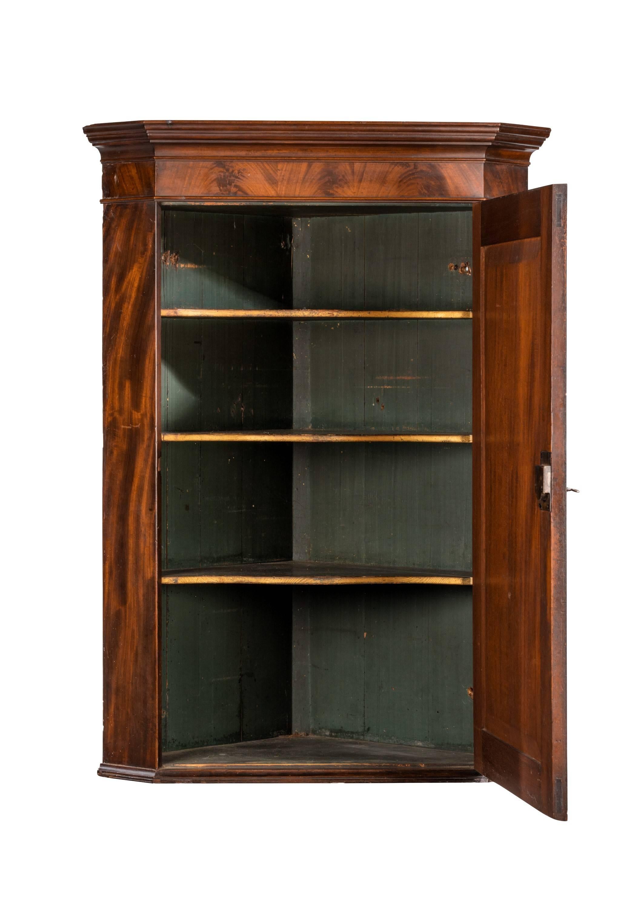 A very finely figured and good quality late George III period mahogany corner cupboard. Flared center panel. Crossbanded in matching timbers. Four shaped shelves to the interior.
