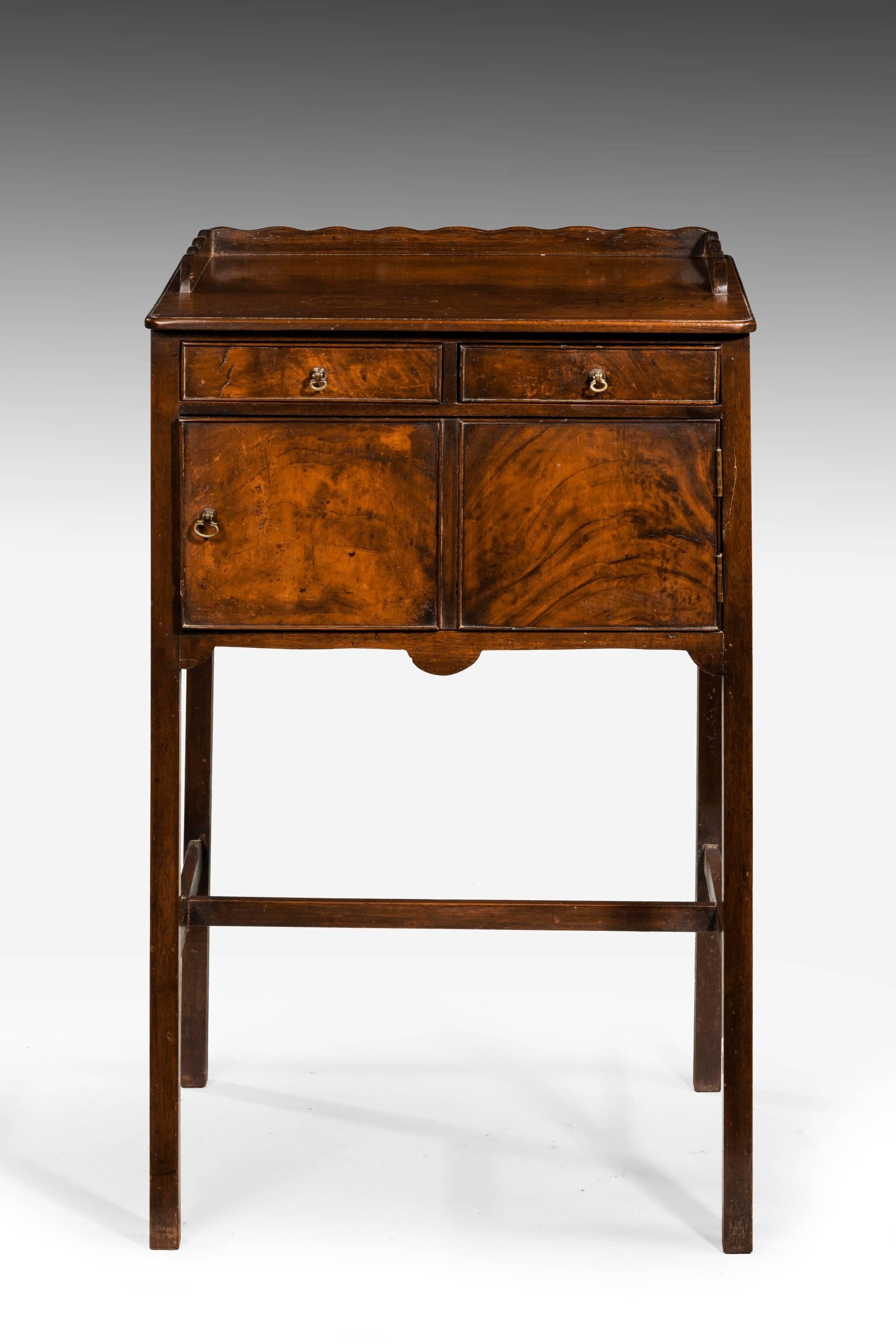 George III period mahogany side cabinet with a shaped top rail. Two slender drawers over a central cupboard. The base with H stretchers on square section supports. Very good color and polish.