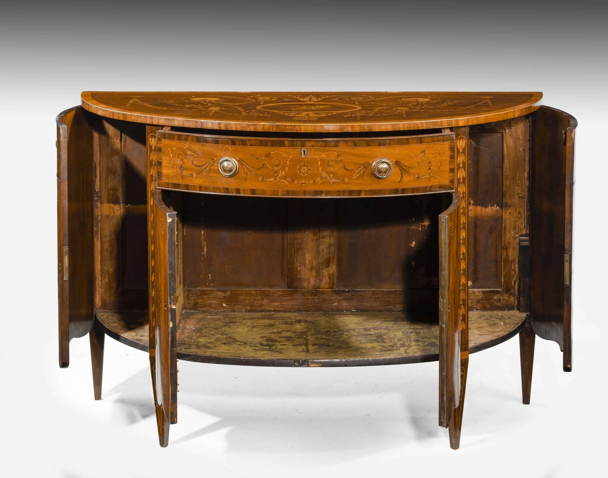 Fine late 18th century mahogany marquetry demilune commode. The beautifully figured timers decorated with inlays and paintwork. The top with swags and central reserve panel. The doors with emblematic decoration of the arts.