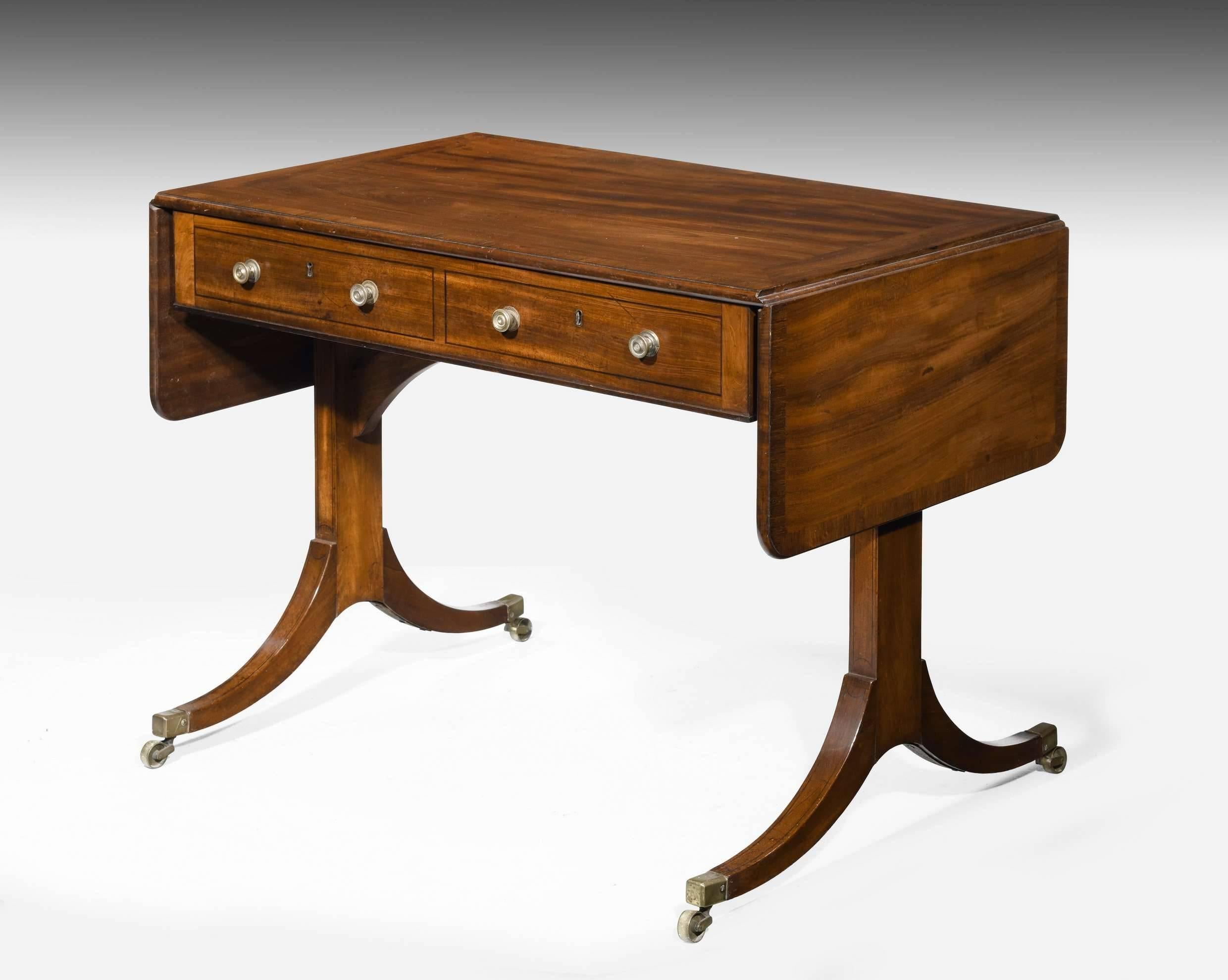 An exceptionally good quality small mahogany sofa table. The beautifully figured top with broad contrasting banding and crossbanding. End supports on flared feet. Excellent overall condition and quality. Retaining original brassware. 

When closed