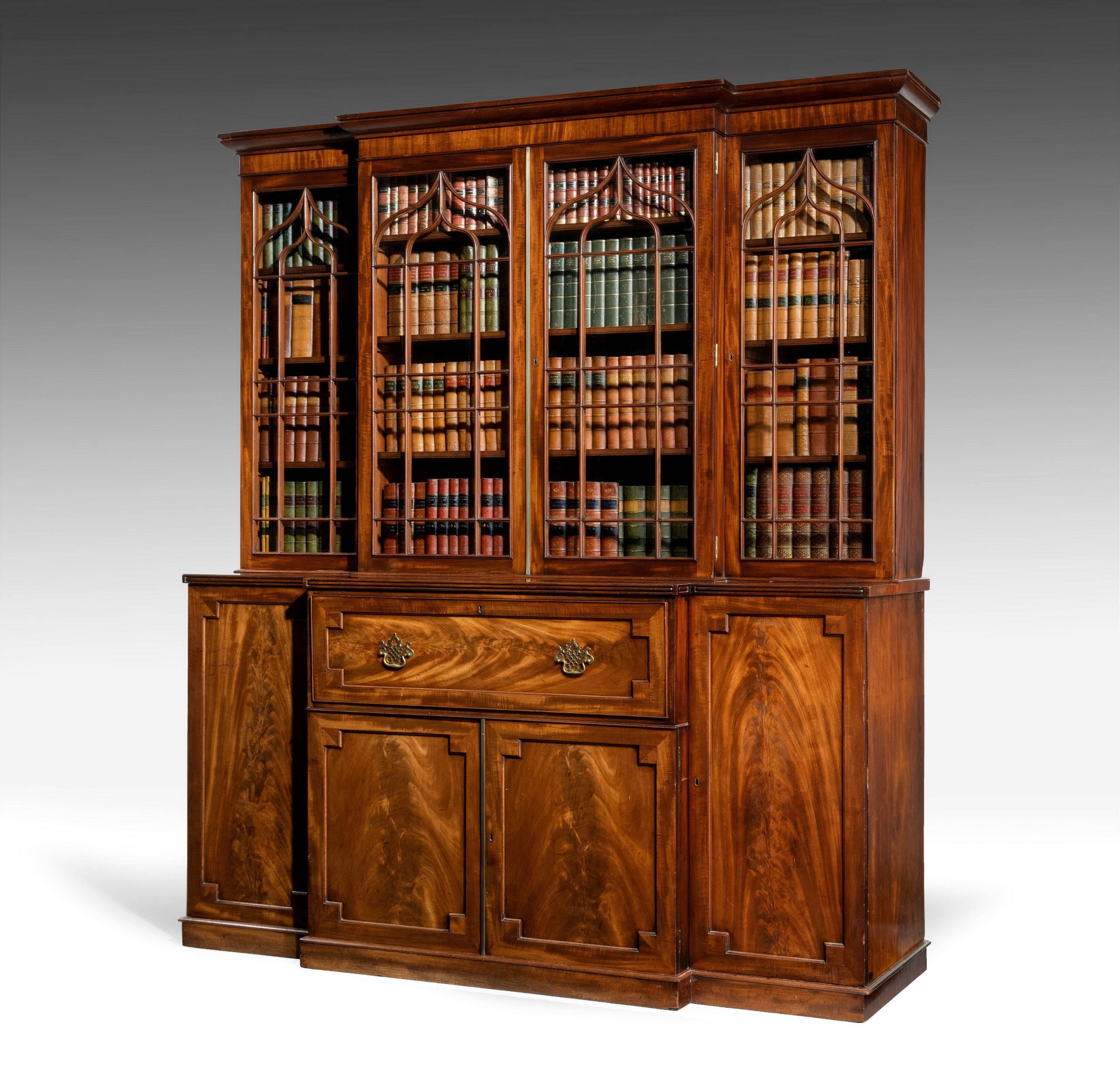 A late Regency period mahogany breakfront bookcase, with Gothic arched glazed doors with adjustable shelves above a well fitted secretaire drawer and cupboards, pierced brass plate handles, on a plinth base. Wonderful flame mahogany panels.