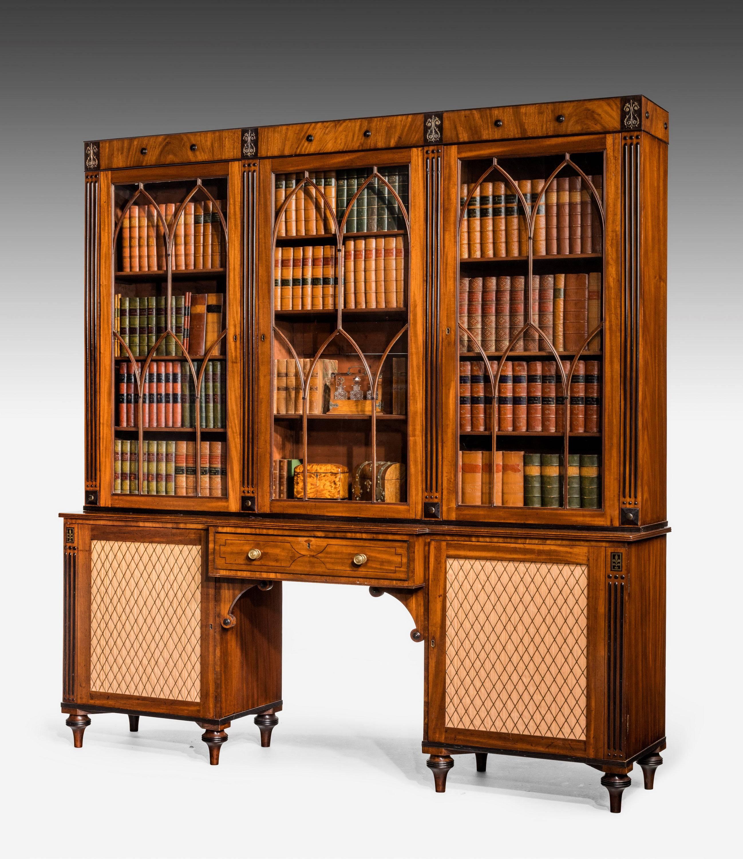 A Regency period mahogany secretaire library bookcase, circa 1820, in the manner of George Bullock, with ebonized and brass inlaid detail, the roundel and stylized lyre mounted frieze above three astragal glazed doors enclosing adjustable shelves,