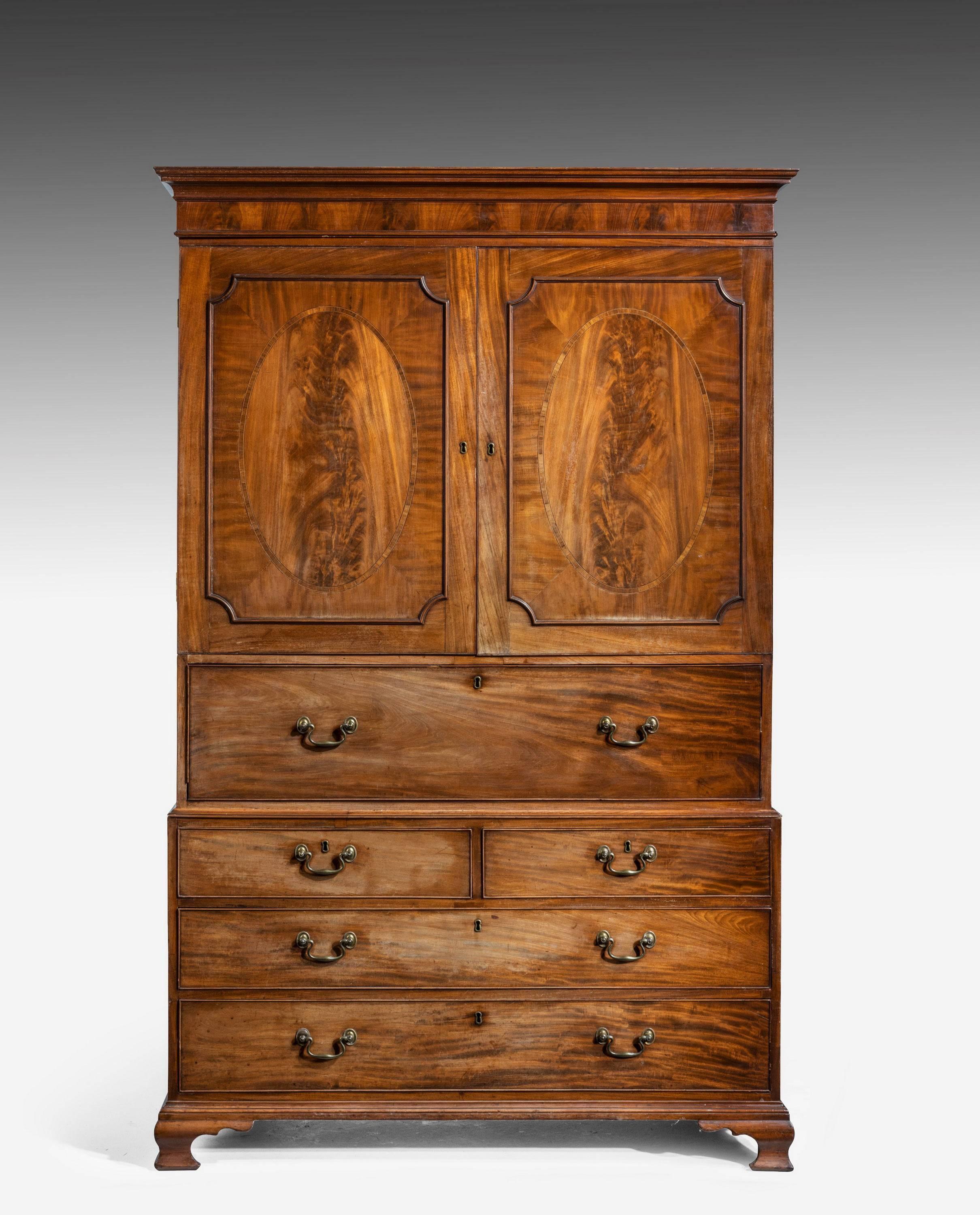 A fine quality George III period mahogany secretaire clothes press. A moulded cornice over a pair of highly figured panelled doors with oval centre sections. The fore front revealing a secretaire with an arrangement of small drawers and pigeon
