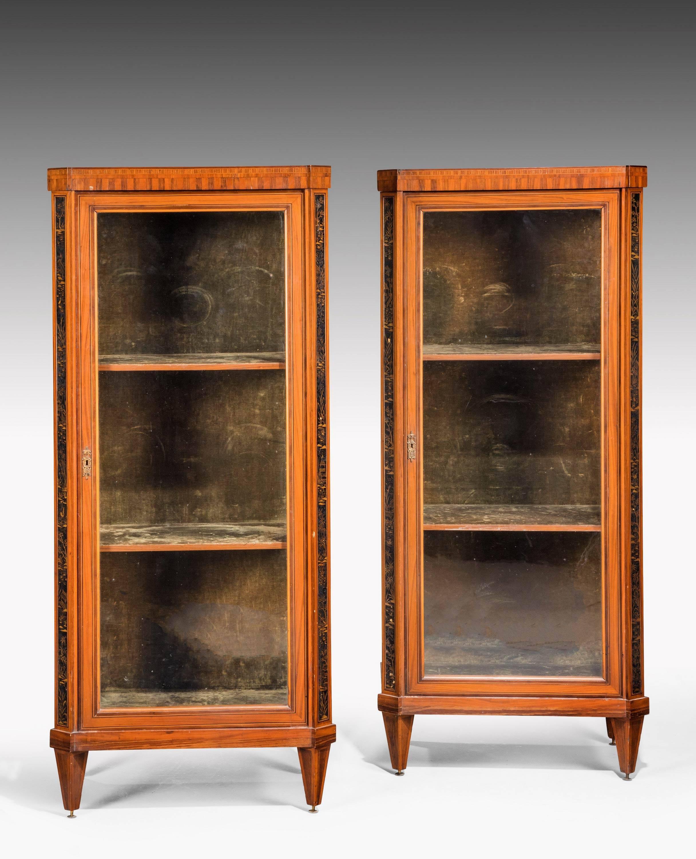 A pair of mid-19th century French Satinwood, black lacquer and gilt japanned Display cabinets in Louis XVI style. Each chequered frieze above the glass panelled door opening to a shelved interior, cornered by slender black lacquer pilasters
