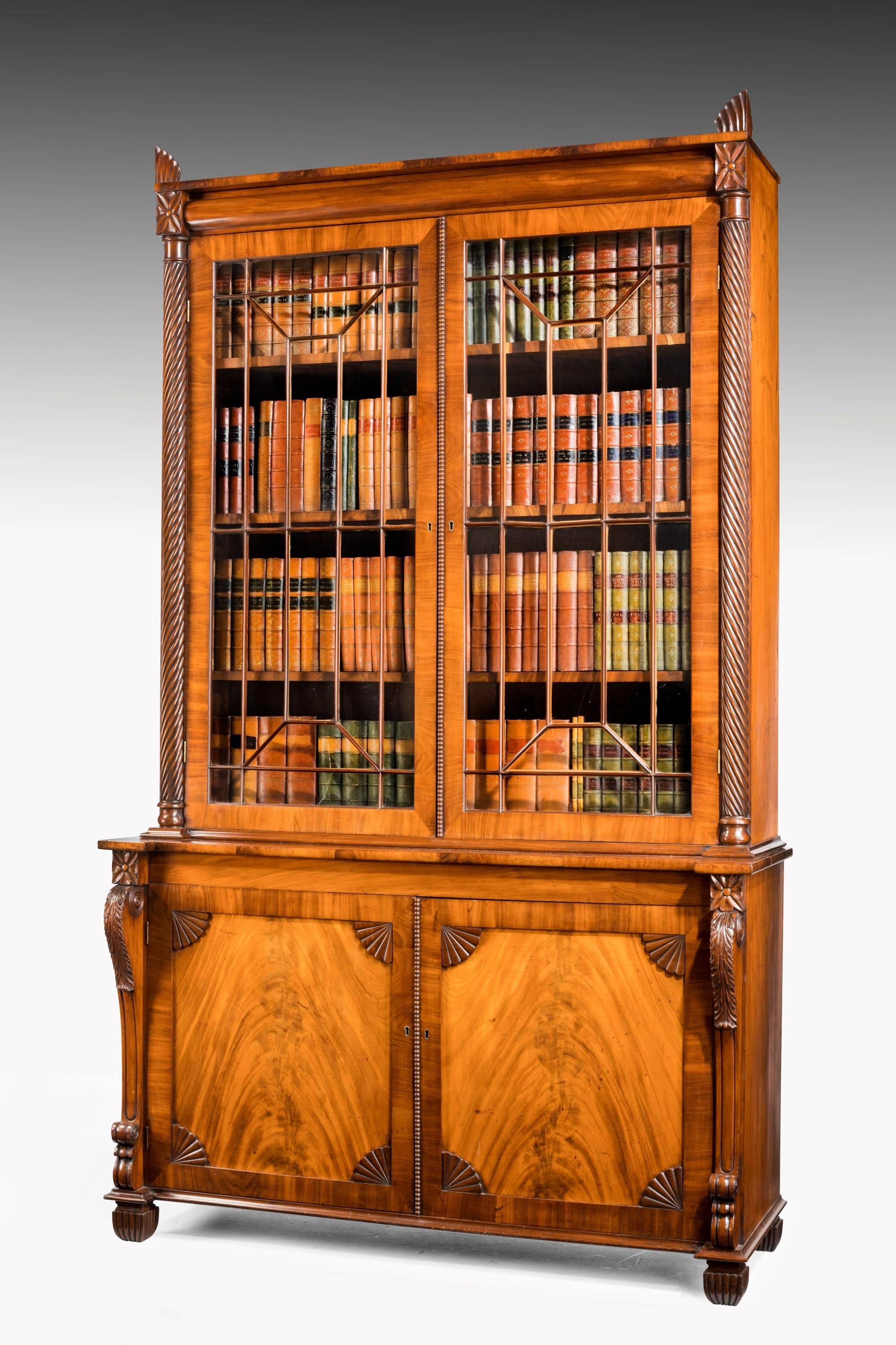 A very well drawn and executed Regency period mahogany bookcase with matching flared panels to the bottom doors with in set shell decoration. The top uprights beautifully written ending in a flared feather type decoration which is all original.