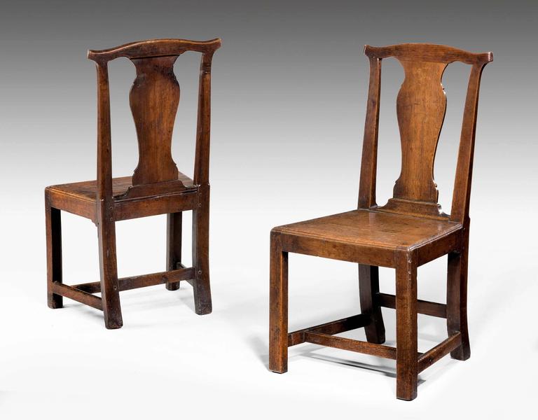 A pair of 18th century country oak side chairs with vase shape back splats on square supports.