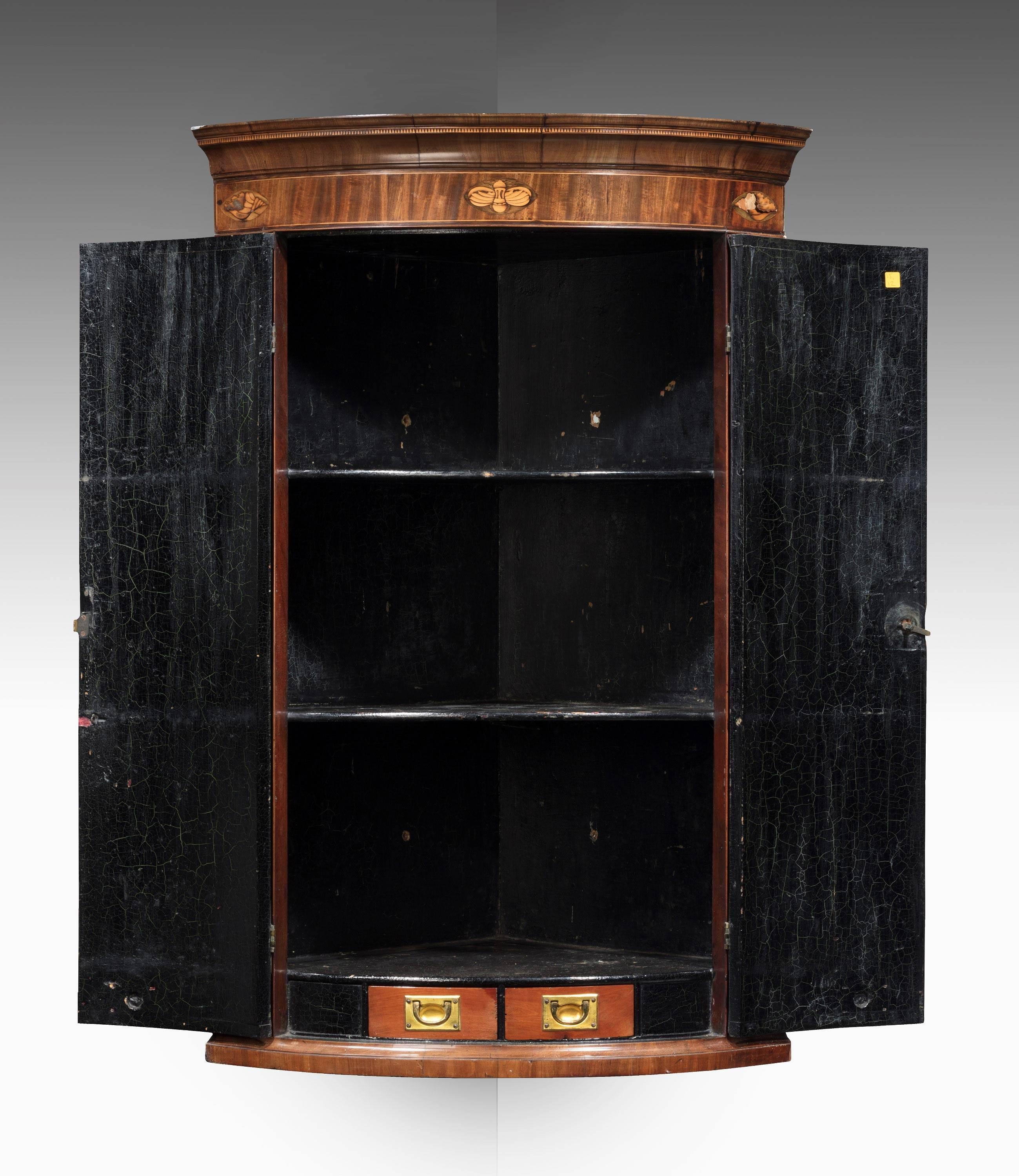 A very good quality mahogany George III period bowfront corner cupboard. Boxwood and satinwood marquetry inlays. The interior incorporating two military type drawers as well as two shelves. Excellent overall condition.