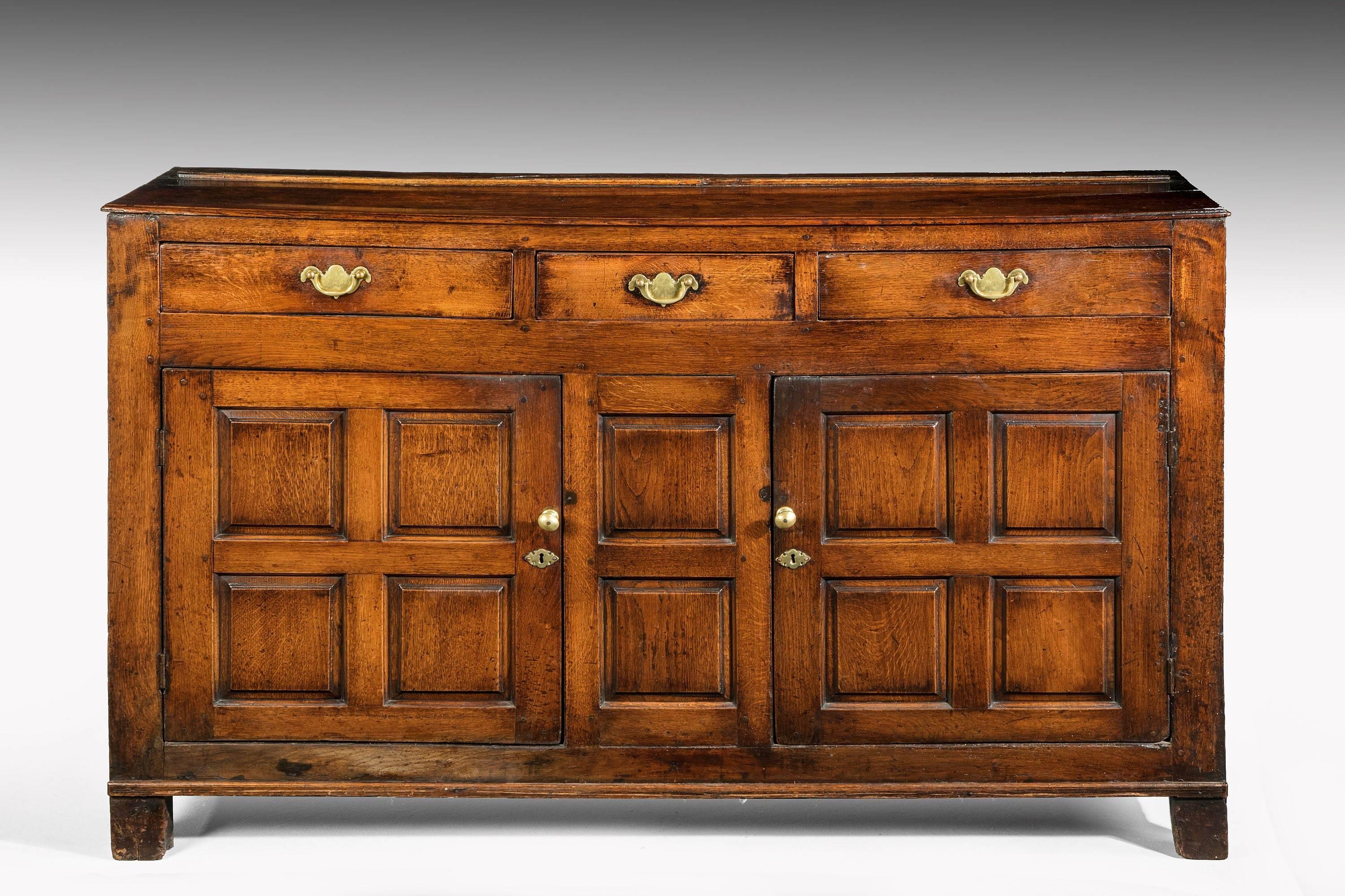 Late 18th century oak dresser base with three drawers to the top above two panelled cupboard doors. The top retaining its original plate support. The whole with attractive details, colour and panelled ends.