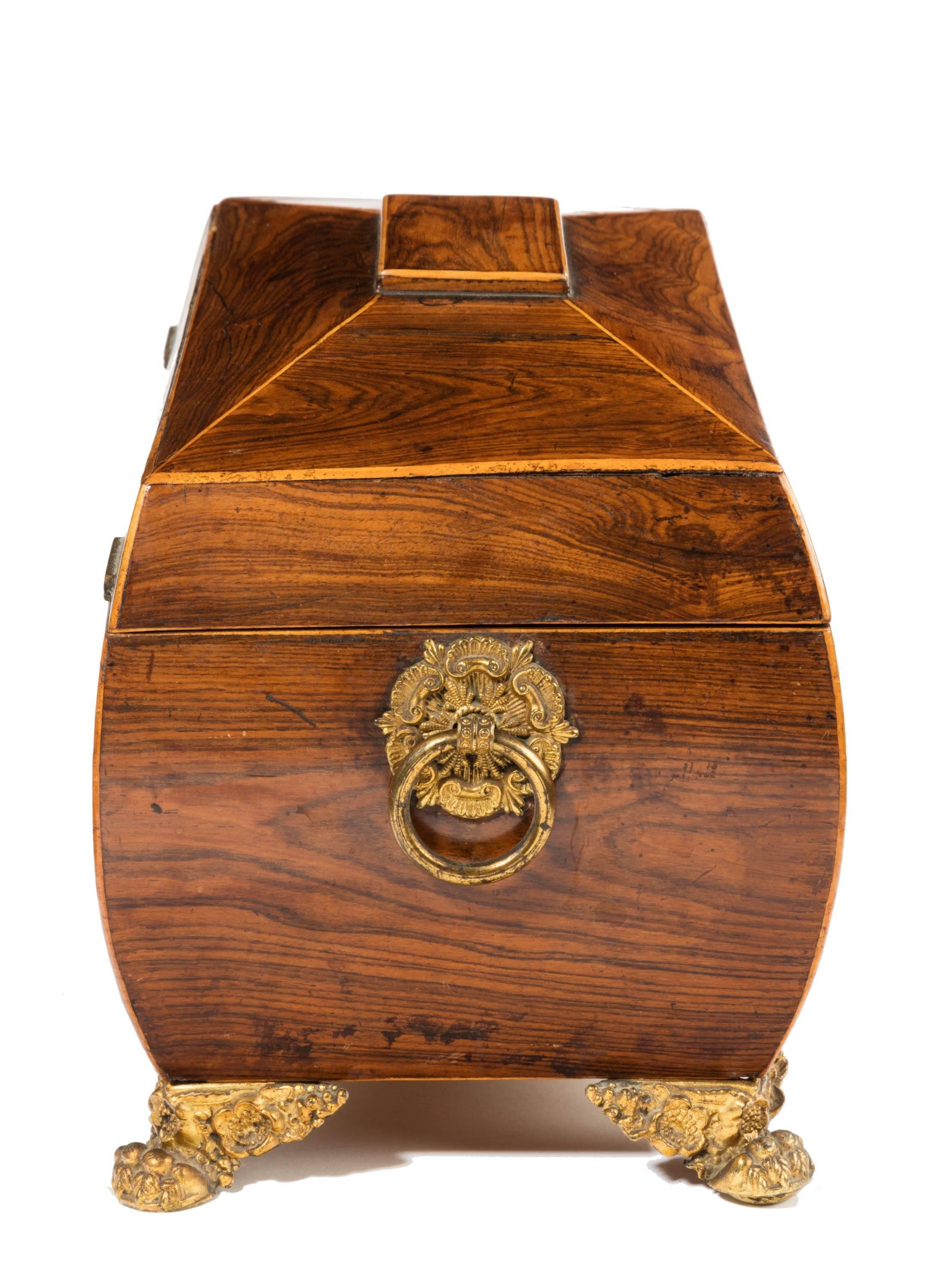 A good Regency period sarcophagus shaped tea caddy. The interior with two fitted lidded compartments but with the central bolt missing. The lid with original pleated silk velvet. Standing on gilt bronze original feet and carrying handles to the