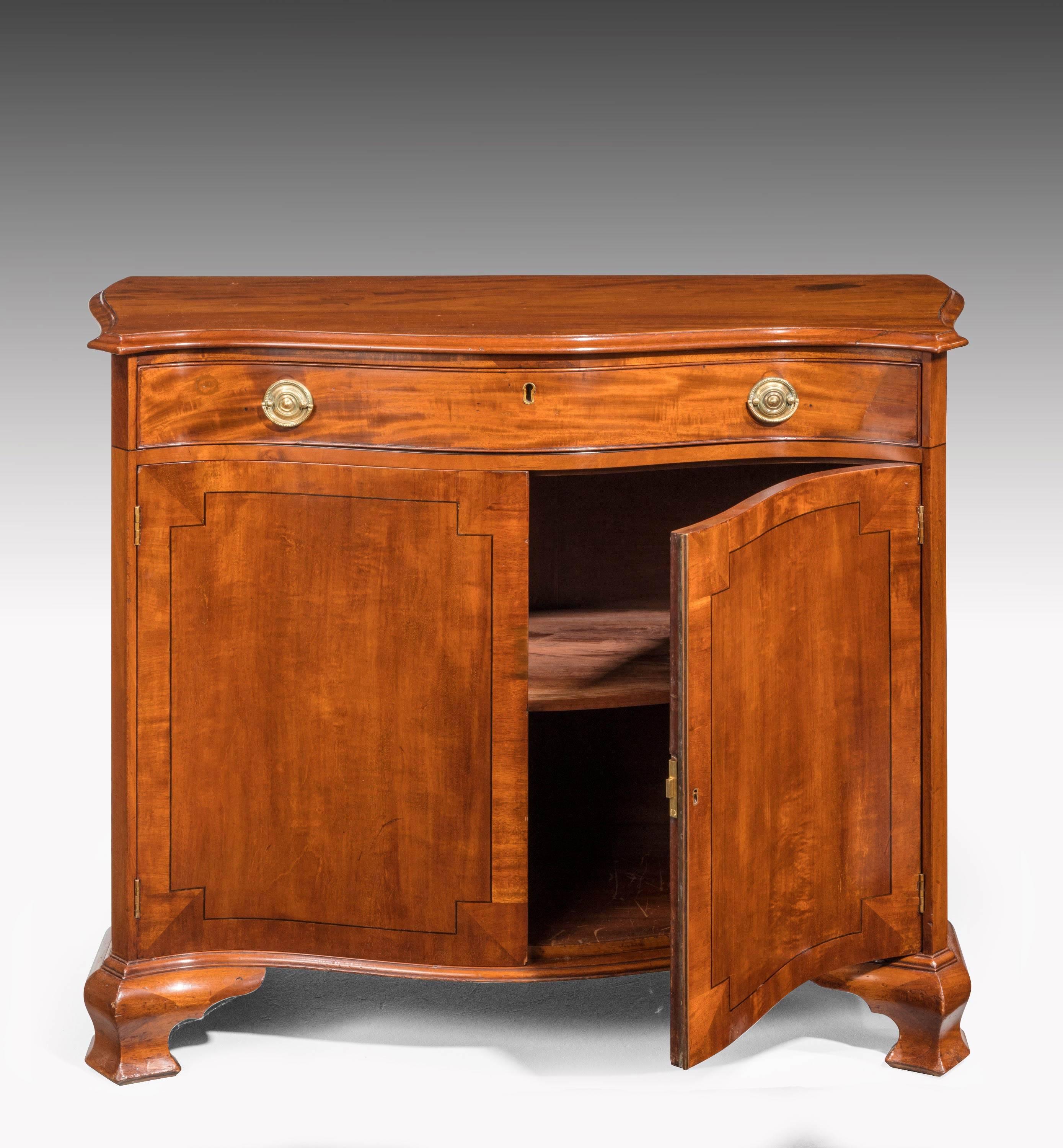 Chippendale period mahogany serpentine side cabinet or commode. On very well-formed ogee bracket feet. The doors crossbanded with inset quartered corners. The drawer retaining period brass.